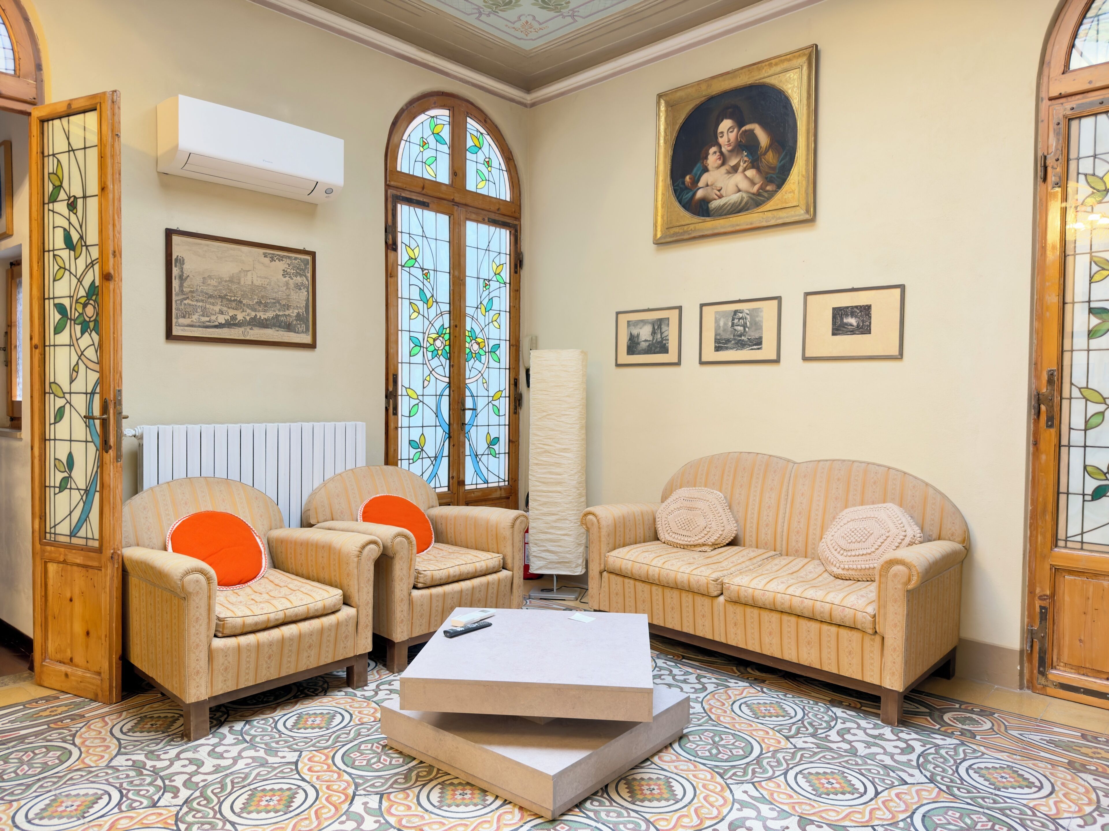 A living room with two armchairs, a sofa, a coffee table, a painting, and a stained glass window.