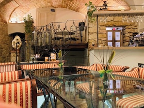 A cozy interior with a glass-top table surrounded by striped sofas, a stone wall, and a rustic staircase. - AlbergoDiffusoVolterra (Volterra)