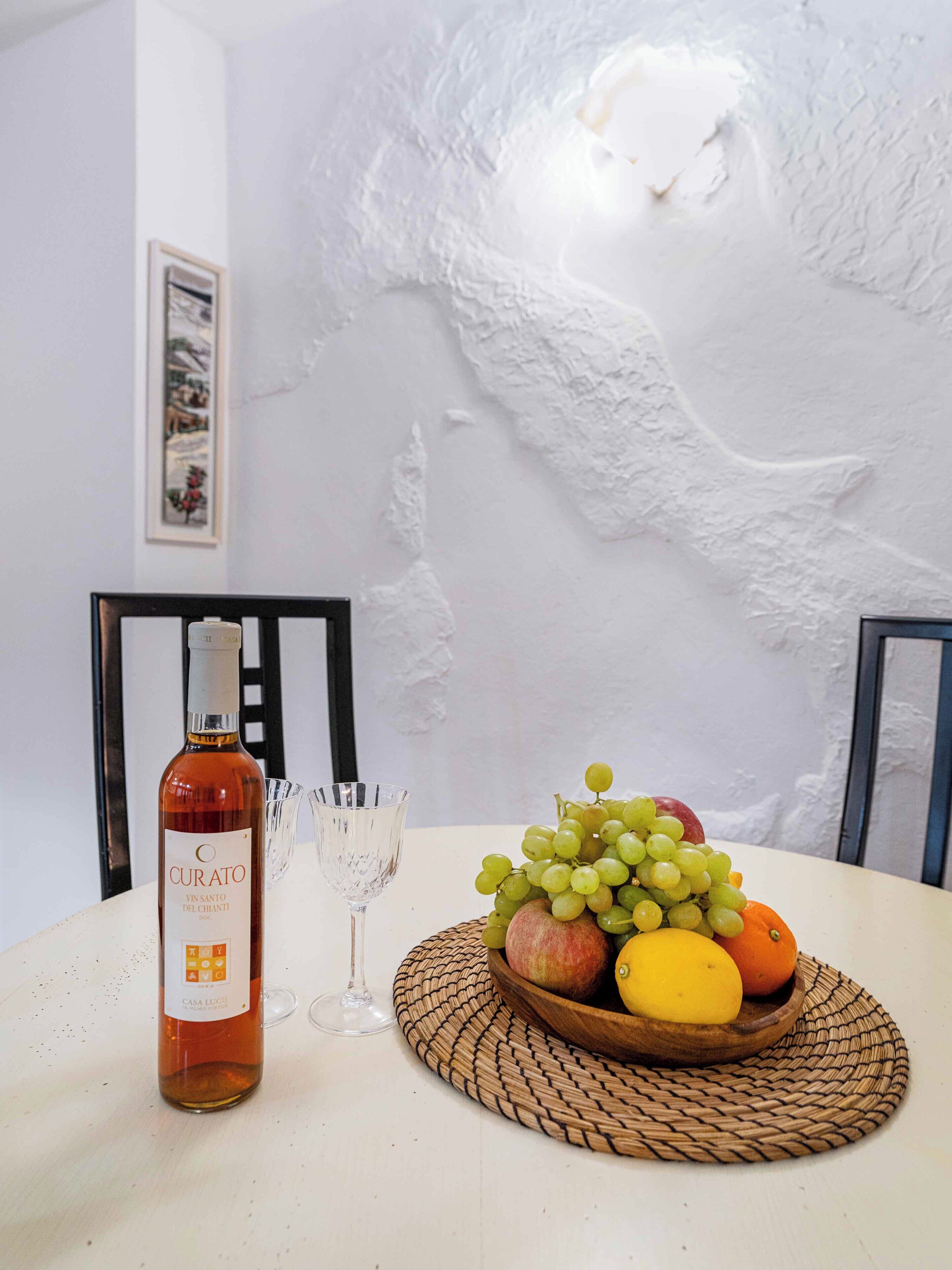 Una mesa con una botella de vino, una copa y un frutero.