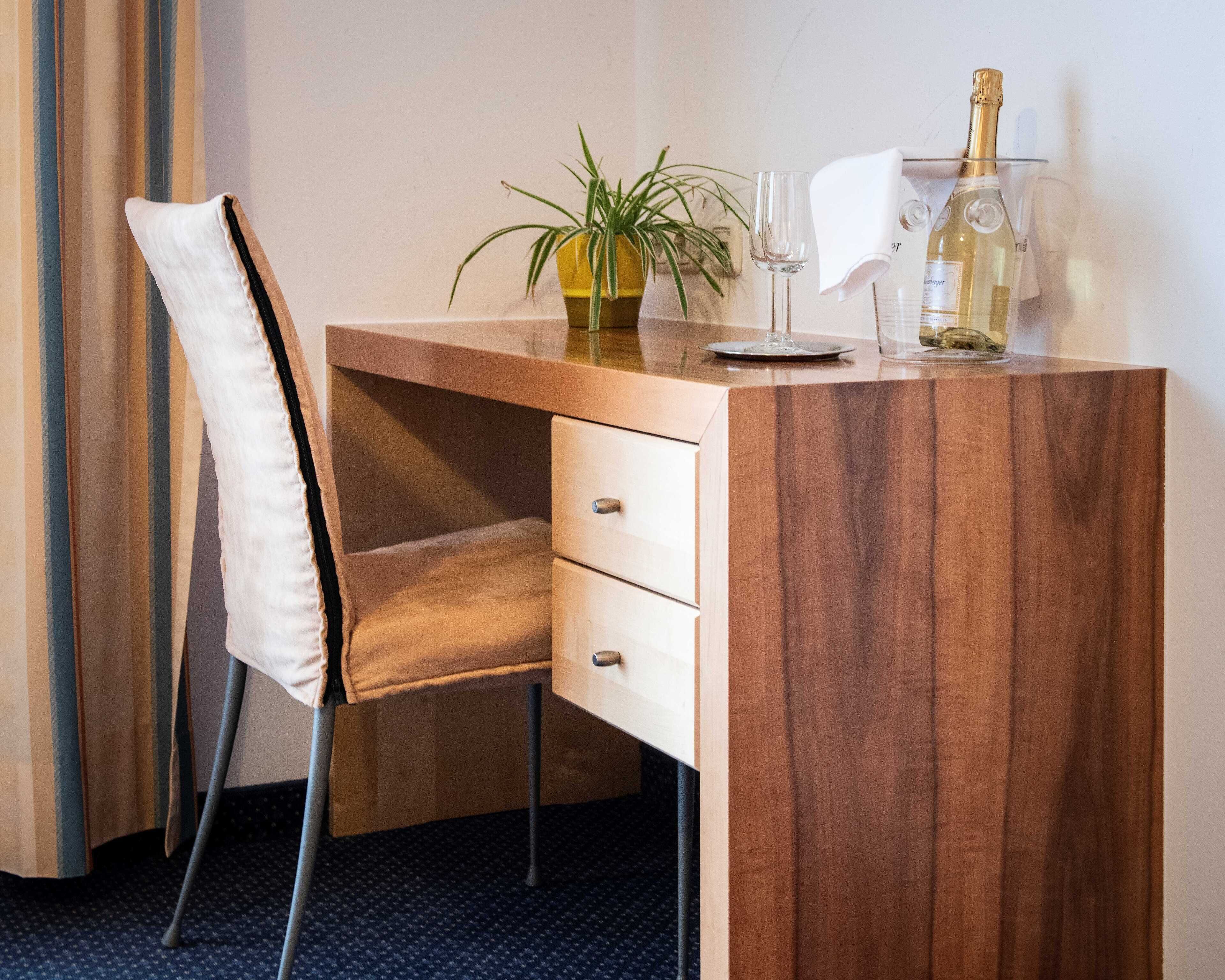 A wooden desk with a chair, a potted plant, a wine glass, and a bottle of champagne.