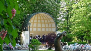 A park with a statue of a seated figure, a gazebo, and people seated on benches. - PARKHOTEL zur KLAUSE (Bad Hall)