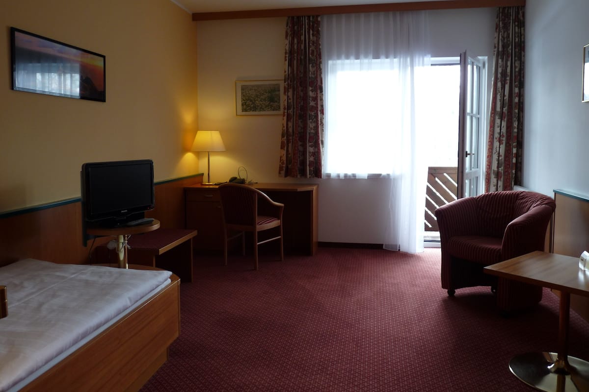 A hotel room with a bed, a desk, a chair, a television, and a window with curtains.