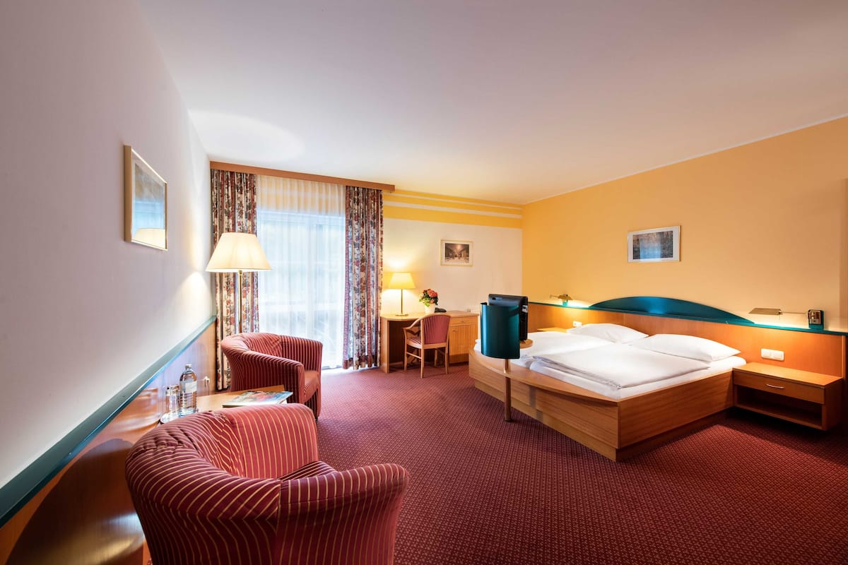 A hotel room with a bed, two armchairs, a desk, a lamp, and a TV.