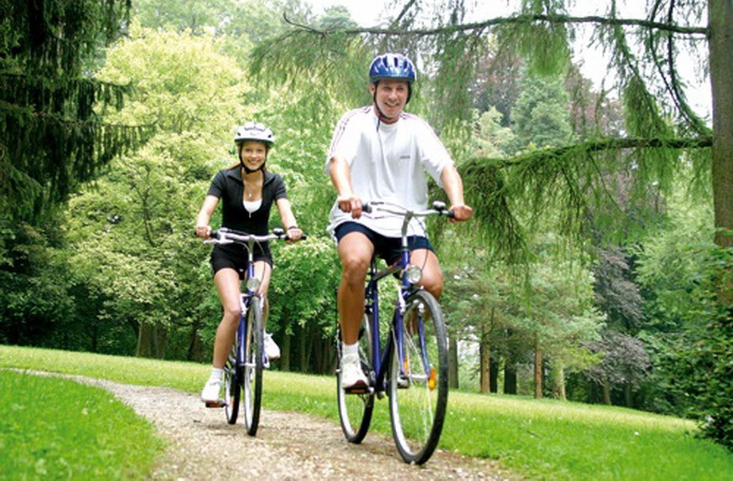 Twee personen fietsen op een grindpad, omringd door bomen.