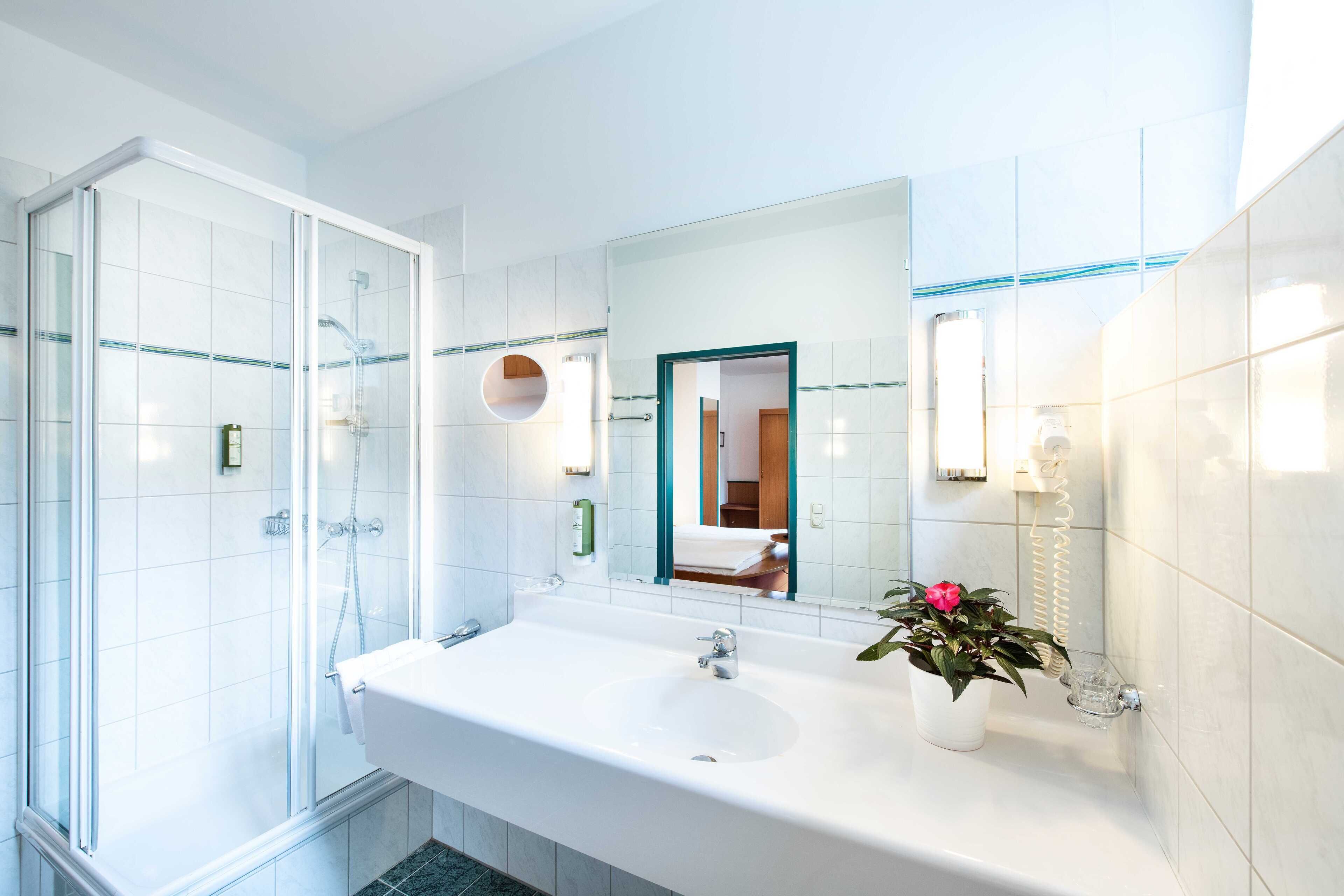 Un baño moderno con ducha envuelta en vidrio, un lavamanos grande de color blanco y una planta en maceta.