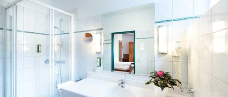 Un baño moderno con ducha envuelta en vidrio, un lavamanos grande de color blanco y una planta en maceta.