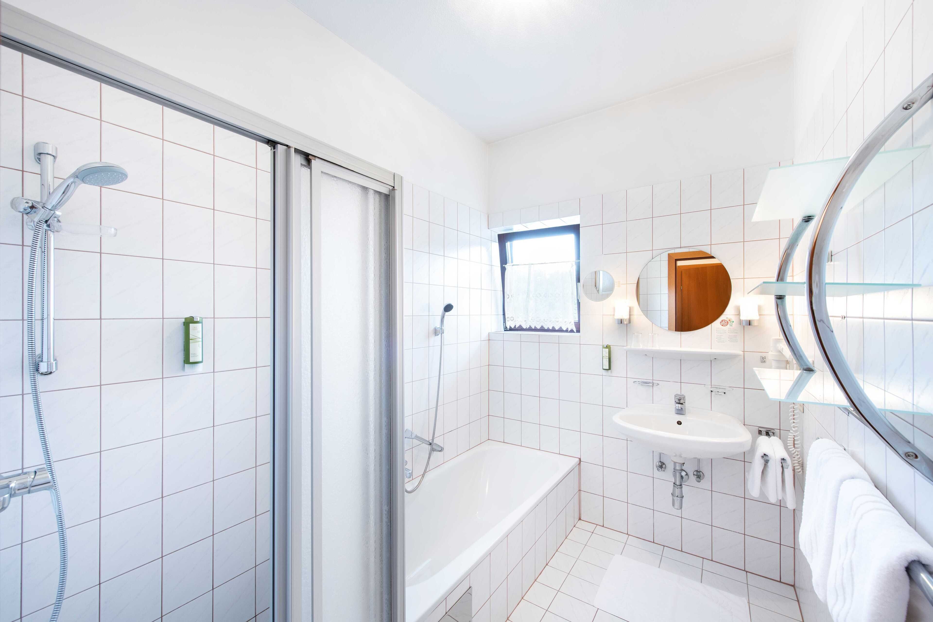 A modern bathroom with a glass shower enclosure, a white bathtub, and a sink with a mirror above it.