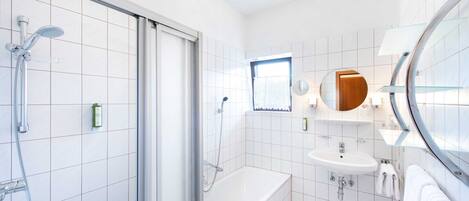 A modern bathroom with a glass shower enclosure, a white bathtub, and a sink with a mirror above it.