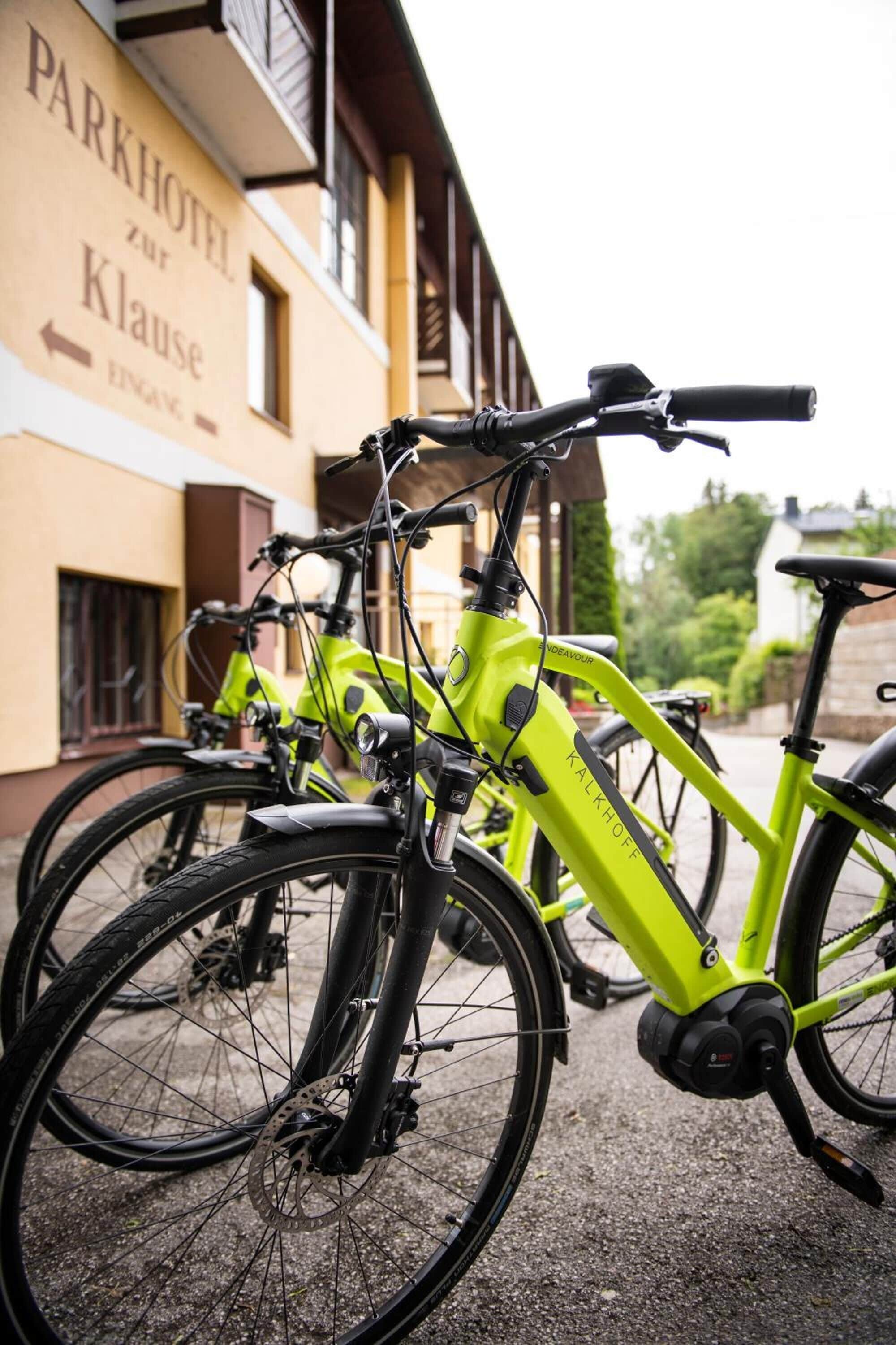 A bright green bicycle parked in front of a building with a sign that reads "Parkhotel zur Klaus".