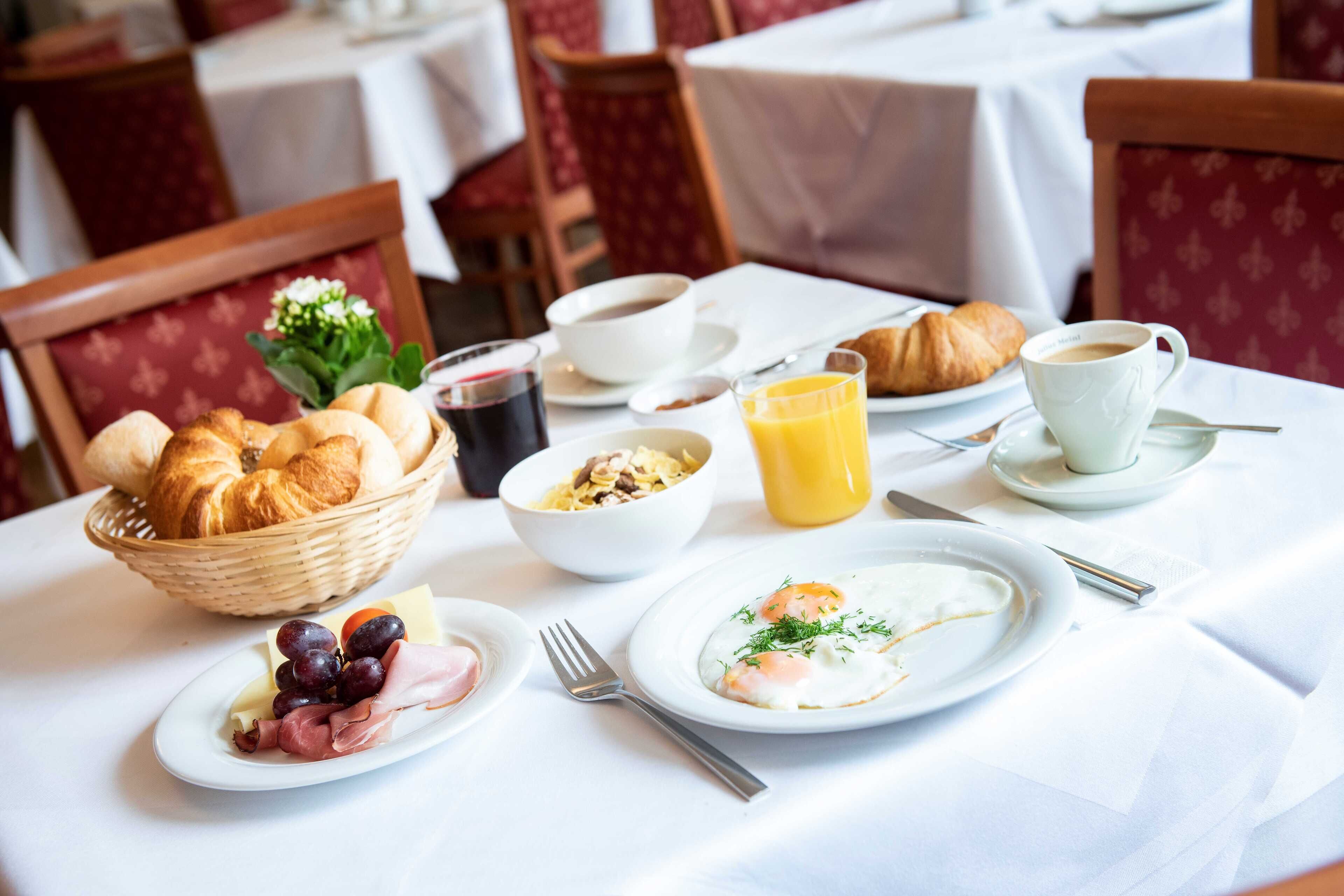 A breakfast setting with croissants, eggs, ham, cheese, and fruit on plates, along with coffee and juice.