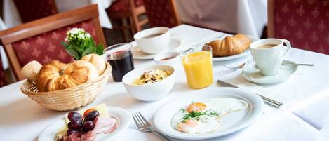 A breakfast setting with croissants, eggs, ham, cheese, and fruit on plates, along with coffee and juice.
