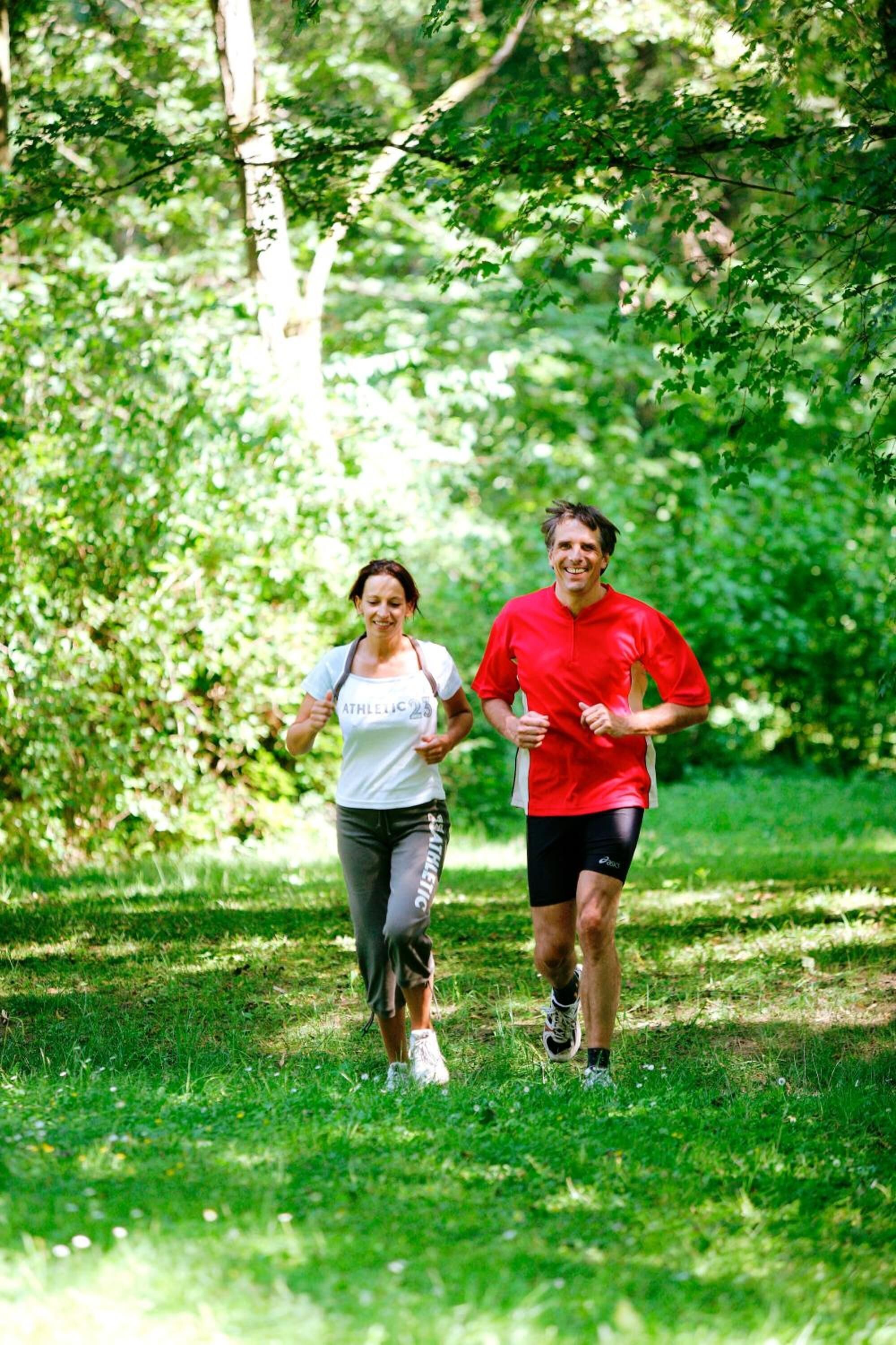 Two people jogging in a park with trees and grass.