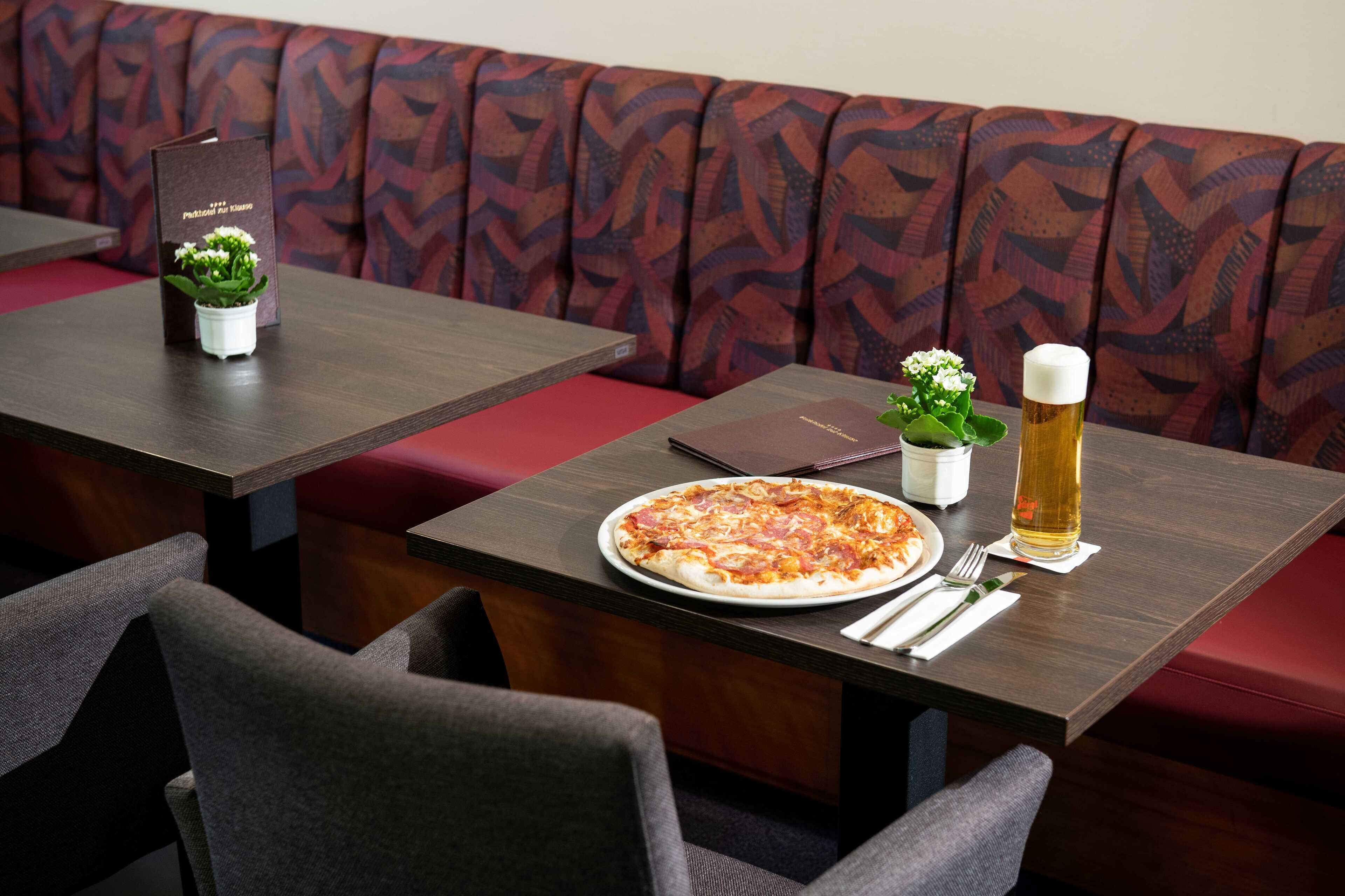 A restaurant setting with a pizza on a table, a beer glass, and a menu.