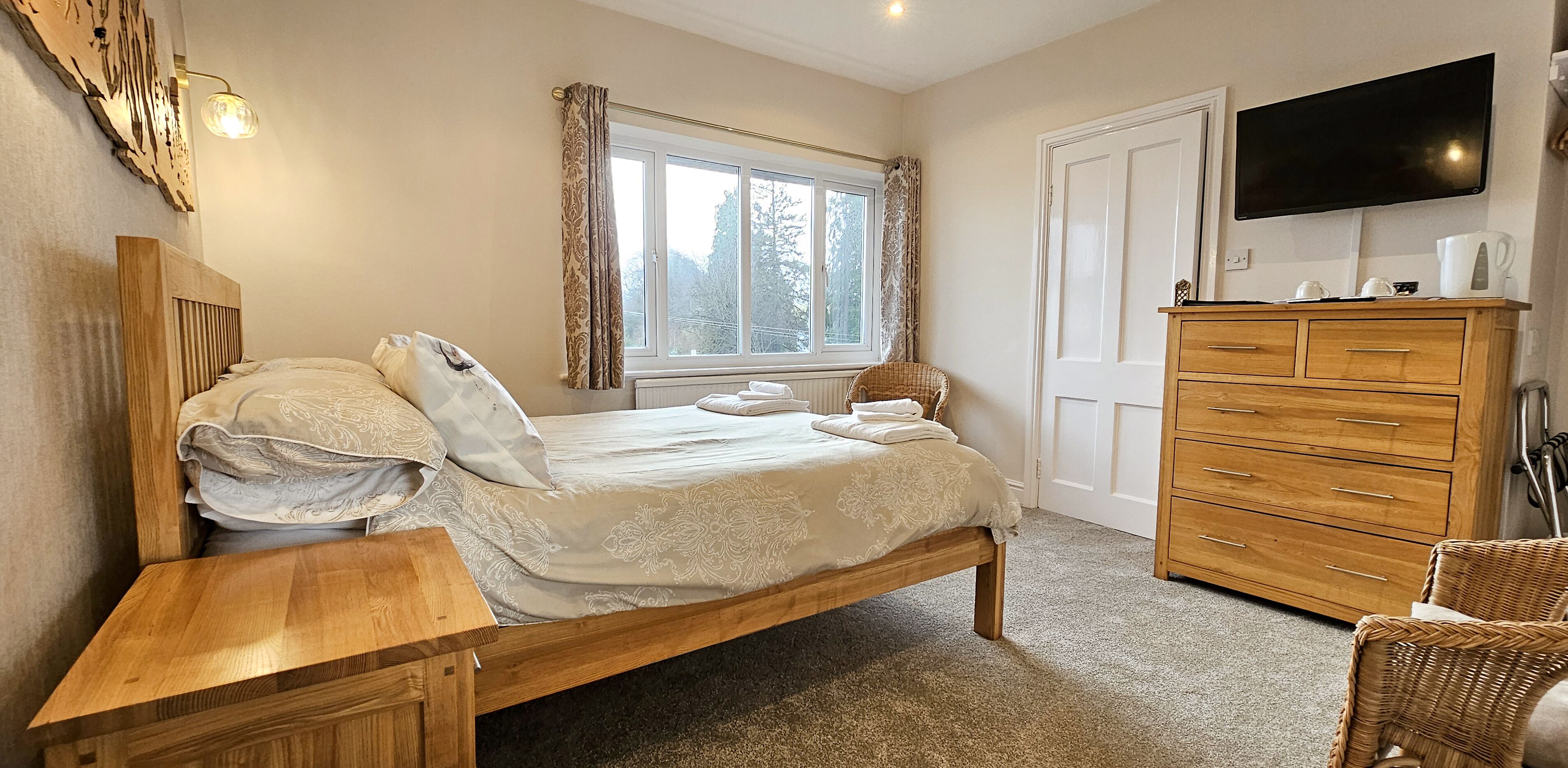 Un dormitorio con una cama de madera, una mesita de noche, un aparador, un televisor y una ventana con cortinas.