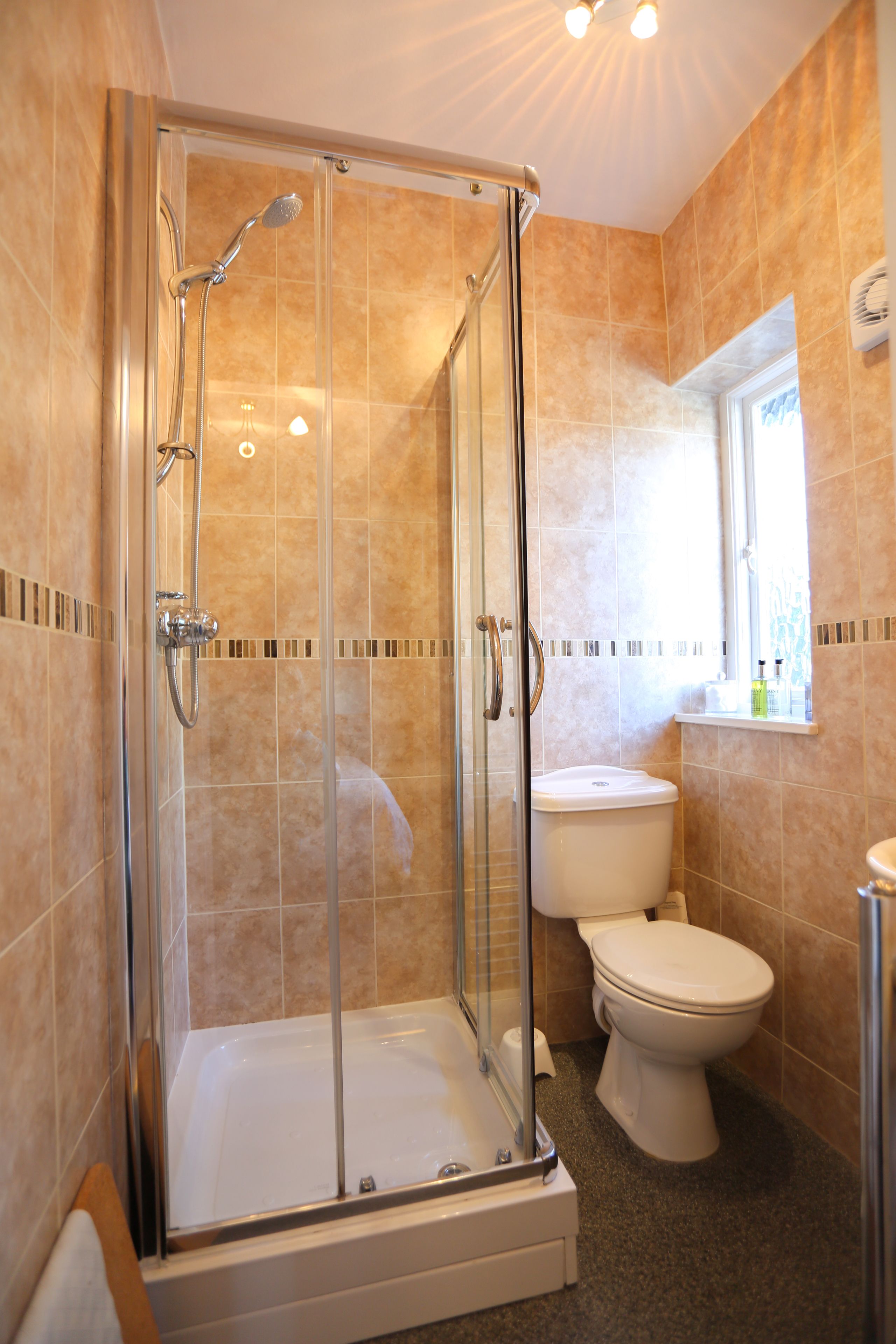 Un baño con ducha de vidrio, inodoro y ventana sobre el lavamanos.