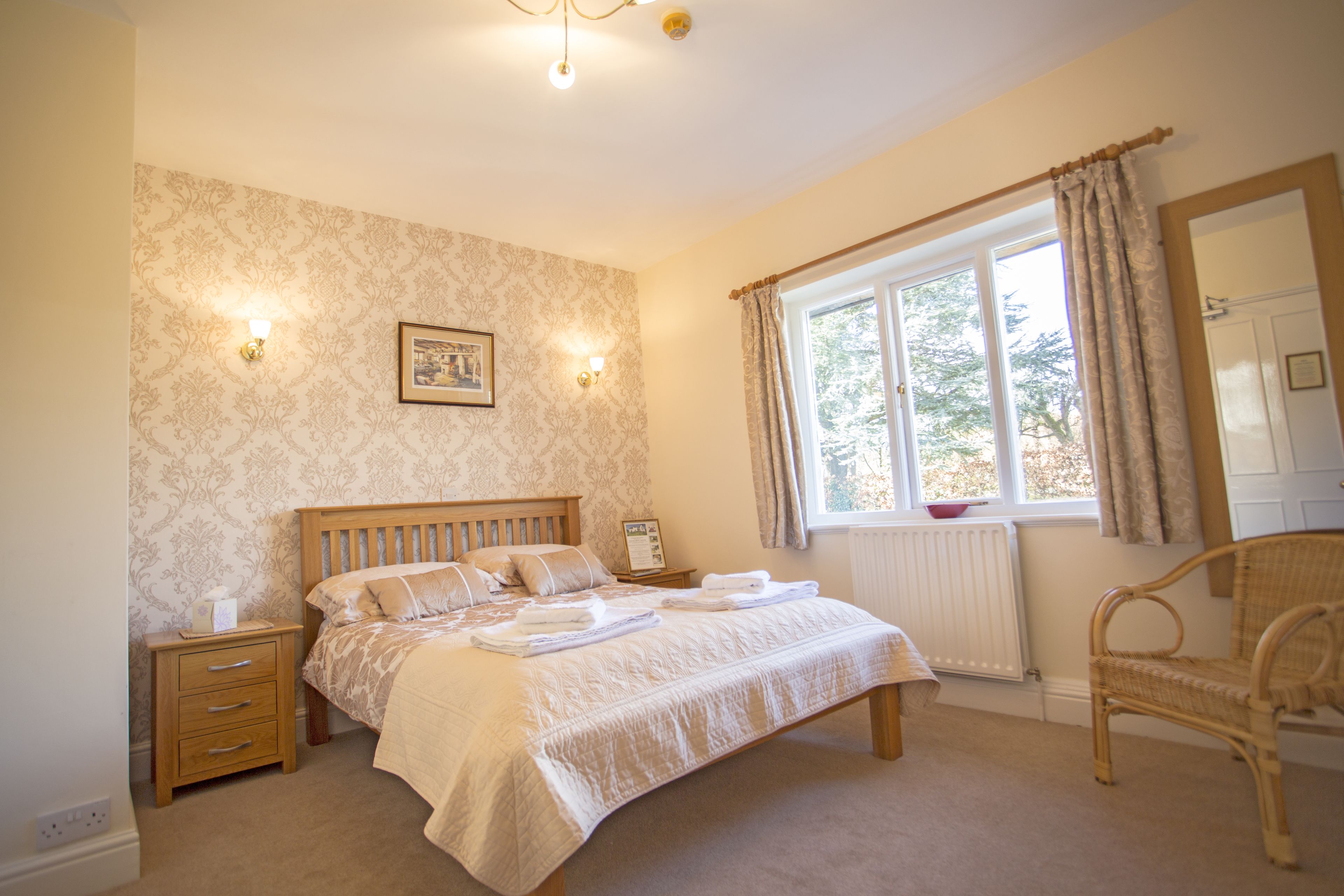 A bedroom with a large bed, bedside tables, a chair, a window with curtains, and wall-mounted lights.