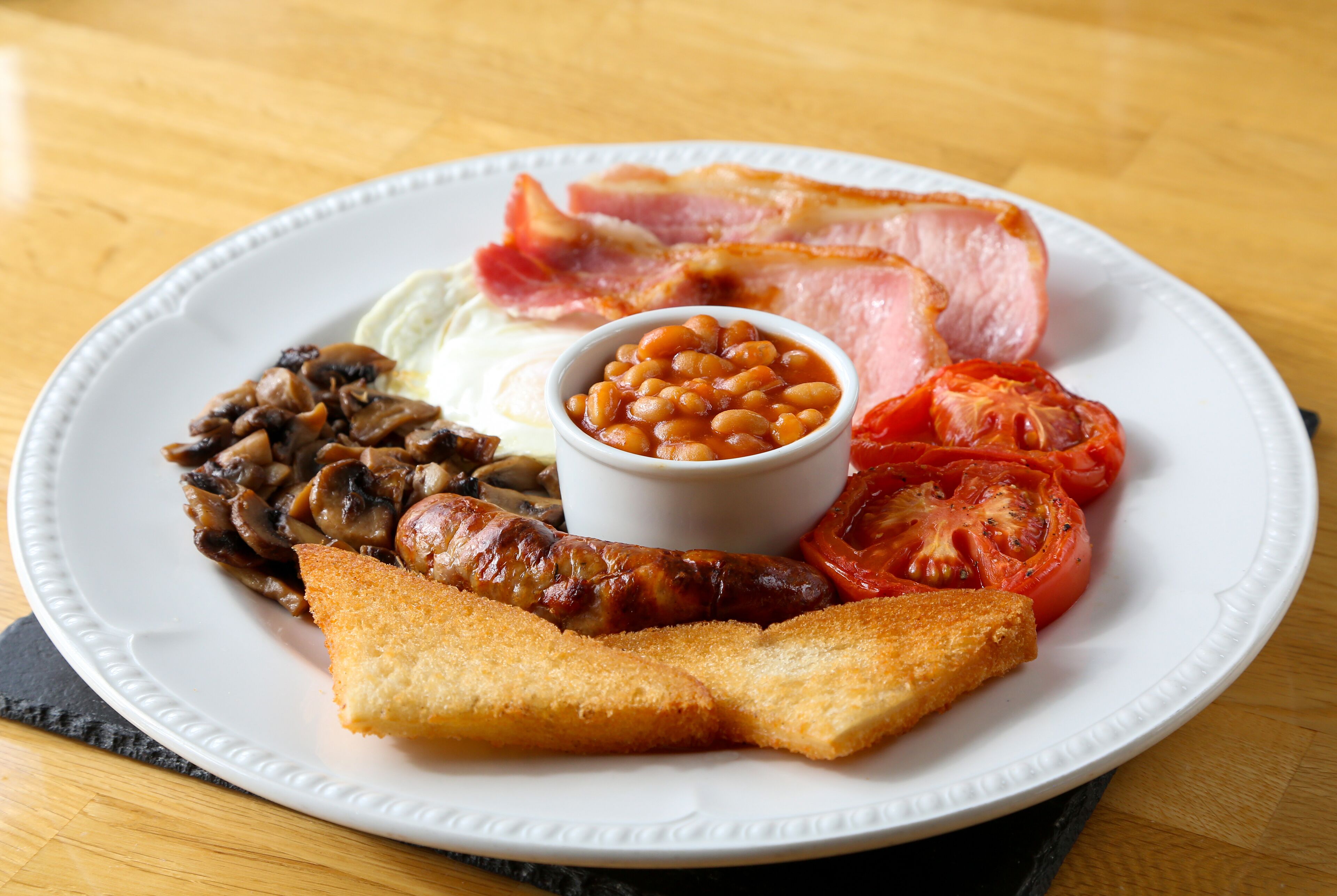 Un plat d'aliments per esmorzar, com ara bacon, ous, xampinyons, fesols, tomàquets i torrades.