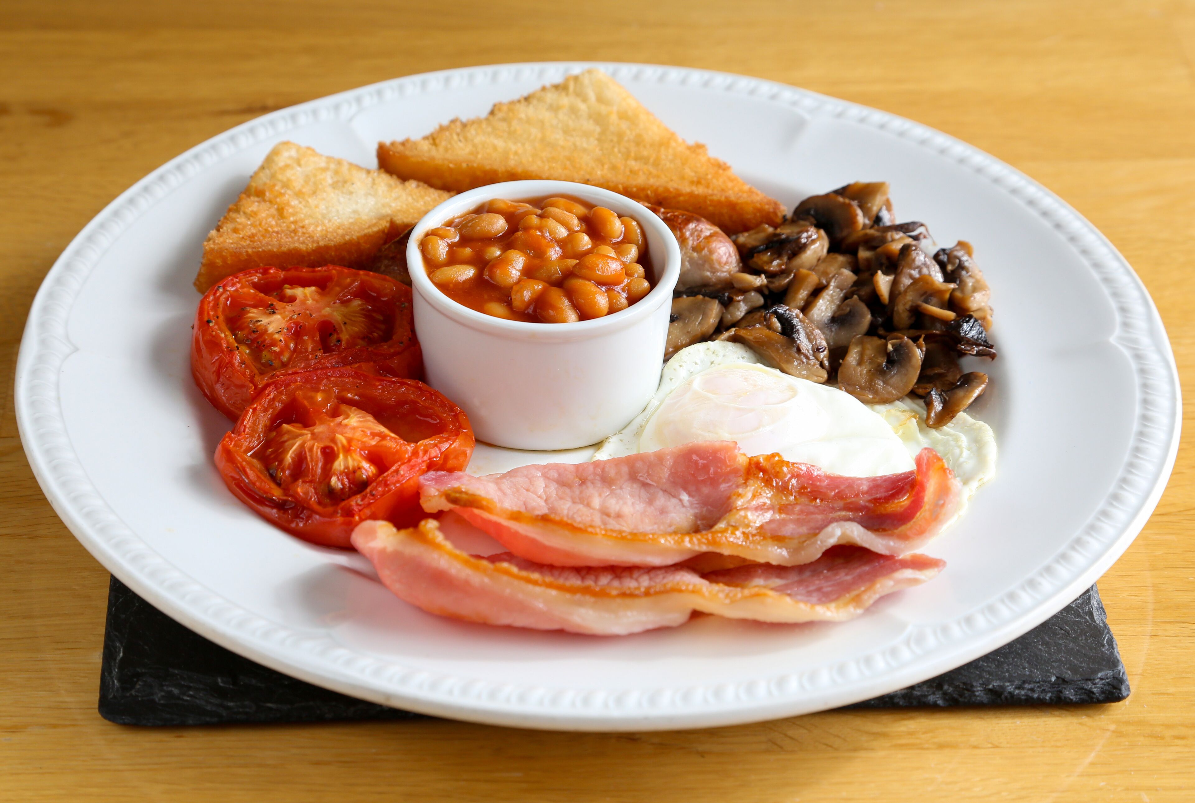 Une assiette de nourriture comprenant des tranches de pain grillé, des haricots, des champignons, des tomates, du bacon et des œufs.