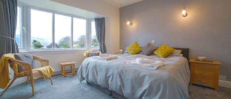 A bedroom with a large bed, a chair, a bedside table, and a window with curtains.