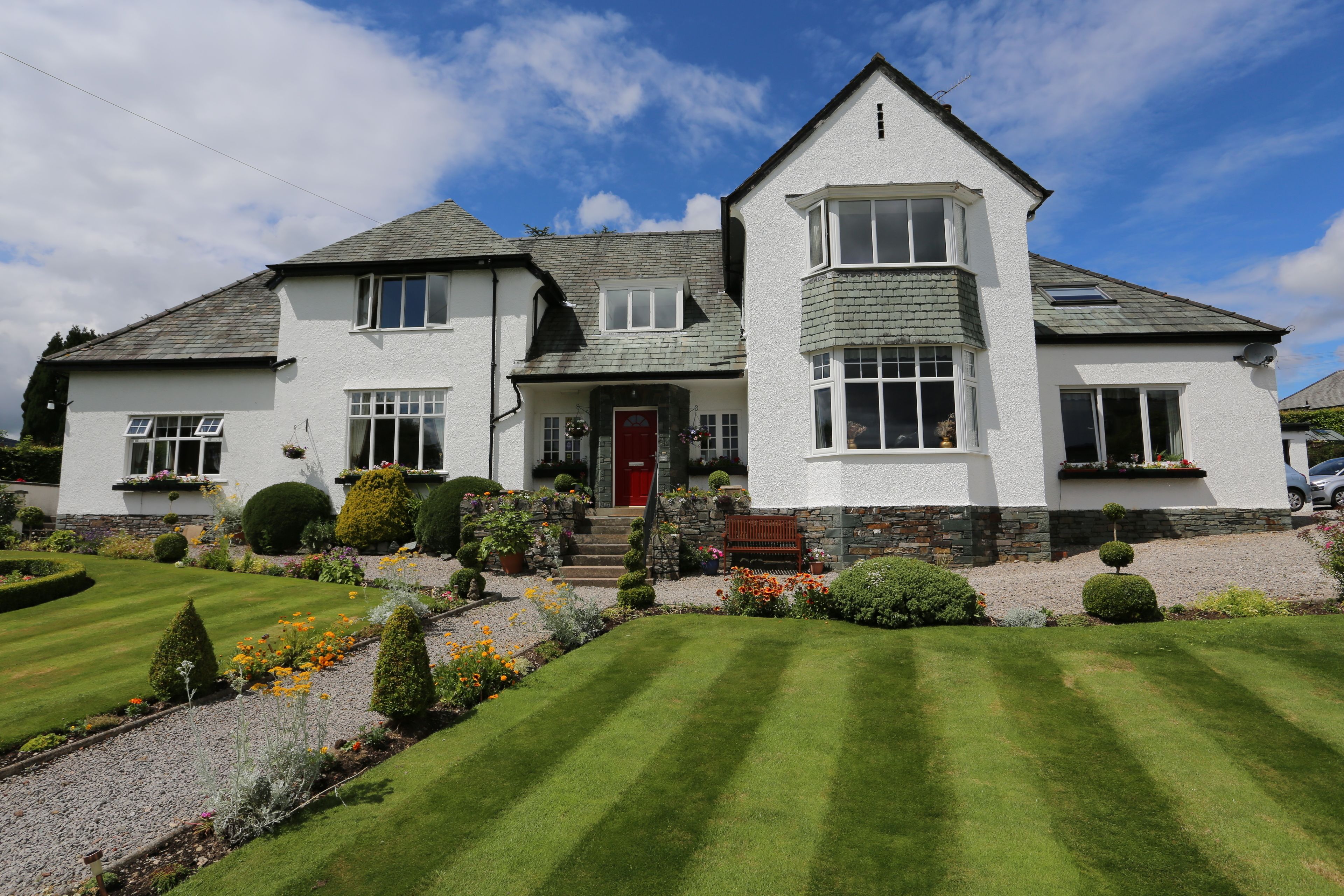 A two-story house with a red door, a stone staircase, and a well-maintained garden.