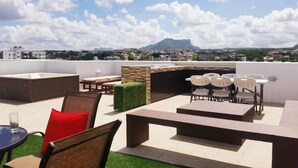 Eine Dachterrasse mit Gartenmöbeln, einem Grillbereich und Blick auf einen Berg und eine Stadt im Hintergrund.