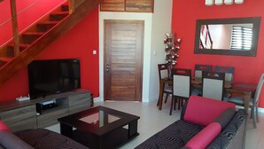 Ein Wohnzimmer mit Treppe, Fernseher, Sofa, Esstisch und Stühlen sowie einer Tür.