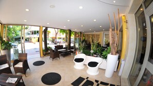 Un vestíbulo de hotel con zonas de estar, ventanas amplias y plantas de interior.