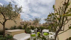 An outdoor seating area with white tables and green stools, surrounded by plants and trees. - B&B Marsala (Marsala)