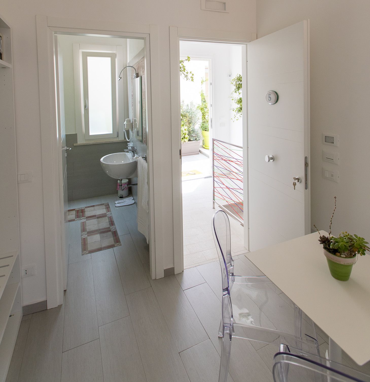 A modern bathroom with a sink, mirror, and shower. There is a potted plant on the counter and a view of a balcony with plants.