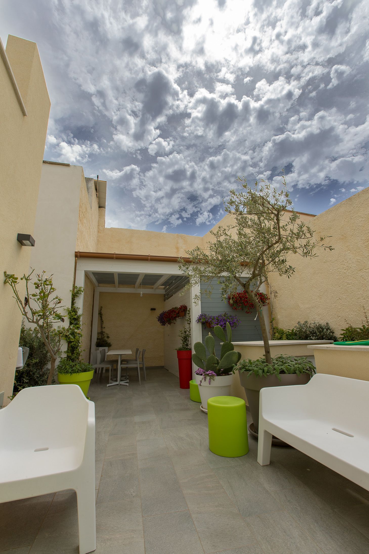 An outdoor patio with white chairs and tables, surrounded by potted plants and a view of the sky.