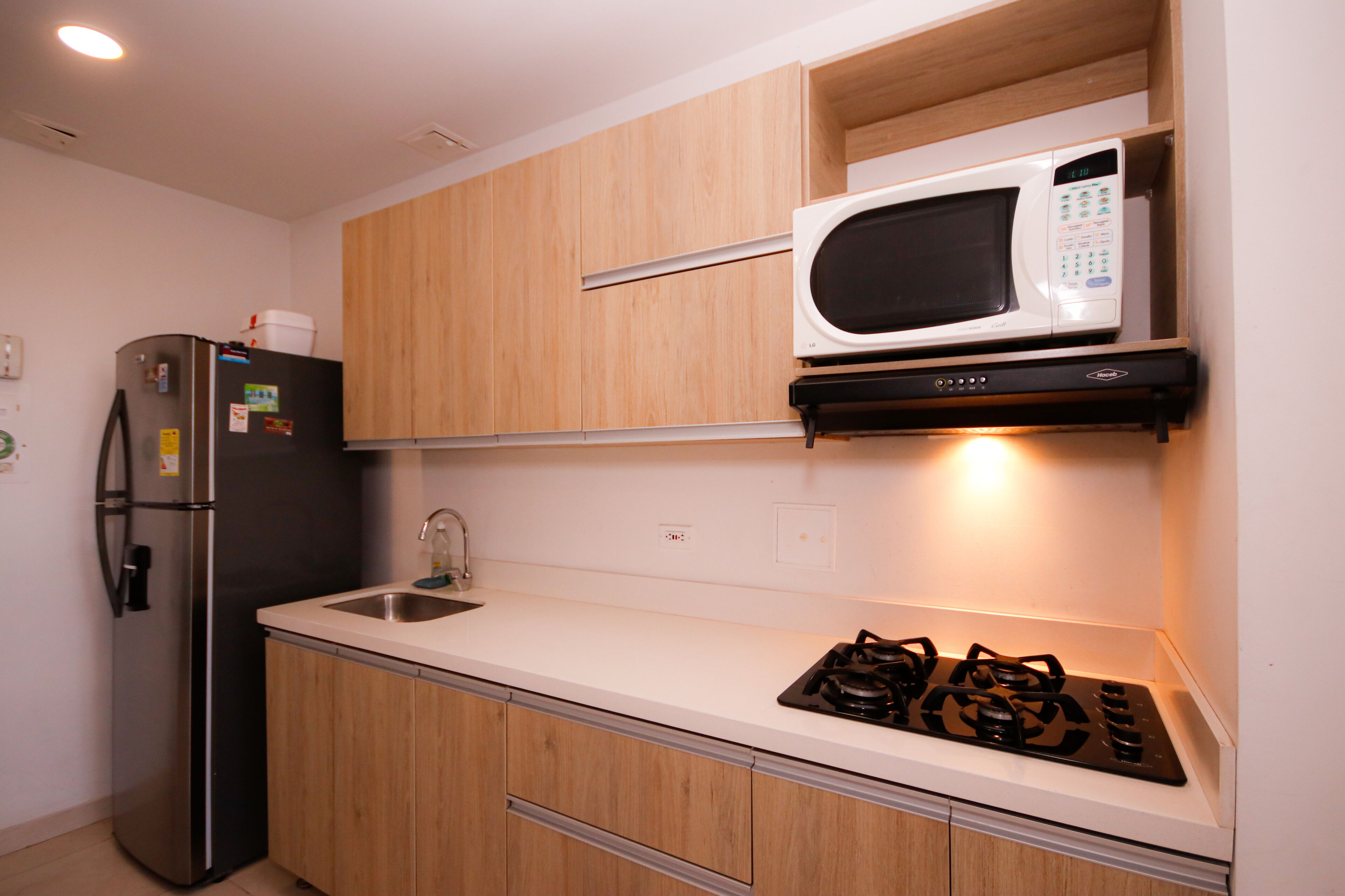 A compact kitchen with wooden cabinets, a stainless steel refrigerator, a microwave, and a gas stove.