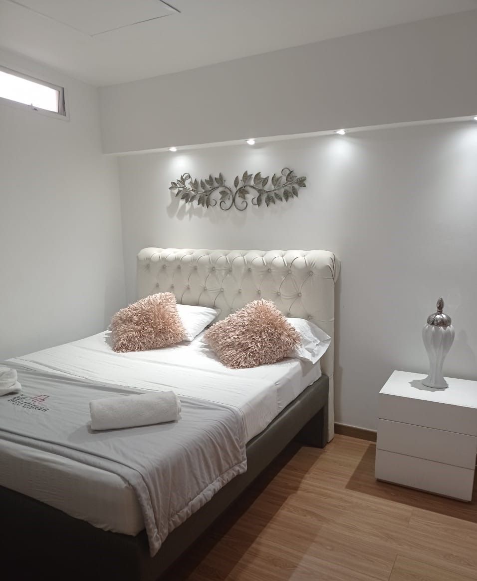 A bedroom with a tufted headboard, two fluffy pillows, a bedside table with a decorative item, and a wall-mounted leaf design.