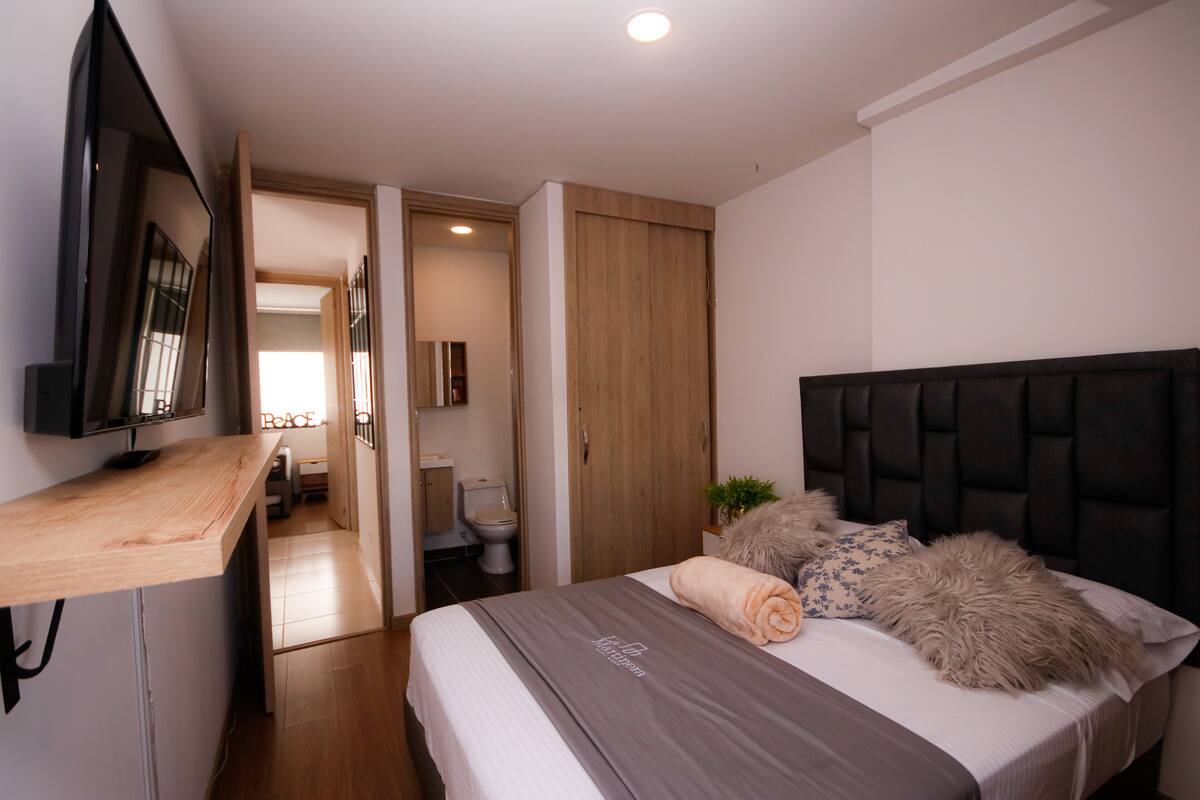 Une chambre à coucher moderne avec un lit, un téléviseur fixé au mur et un bureau en bois.