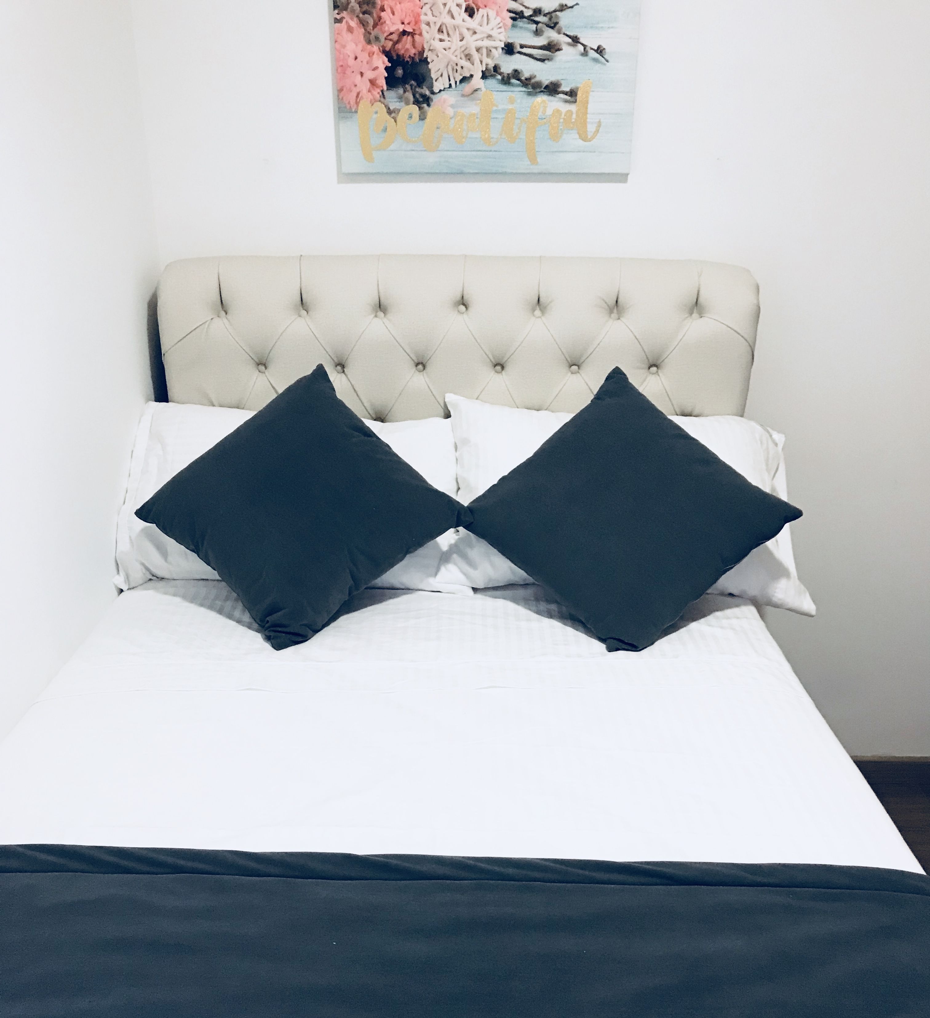 A bed with a tufted headboard, white bedding, and two dark pillows.
