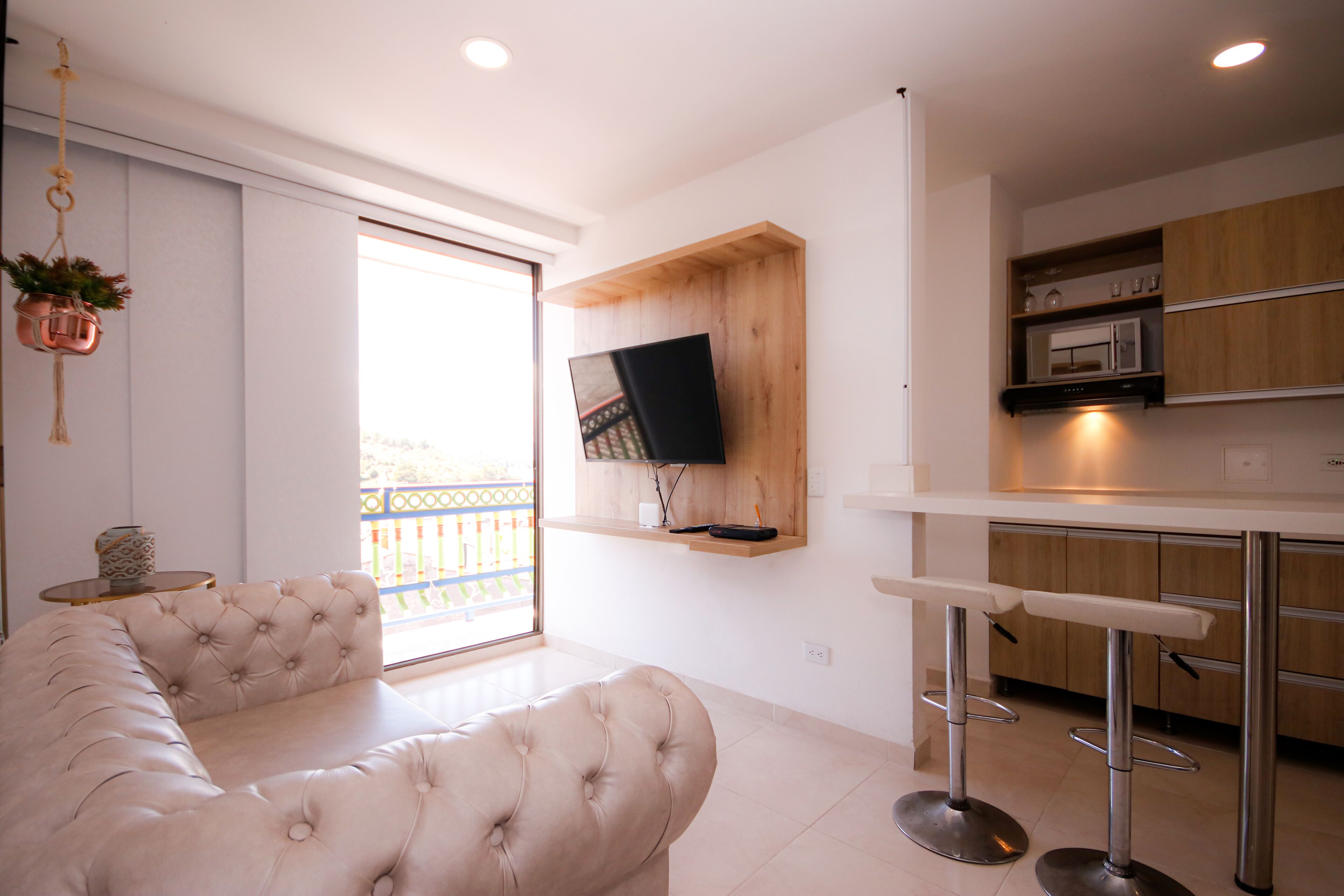 Un salon moderne avec un grand canapé beige, un téléviseur fixé à un mur en bois et un coin cuisine doté de meubles en bois et d’un tabouret de bar.