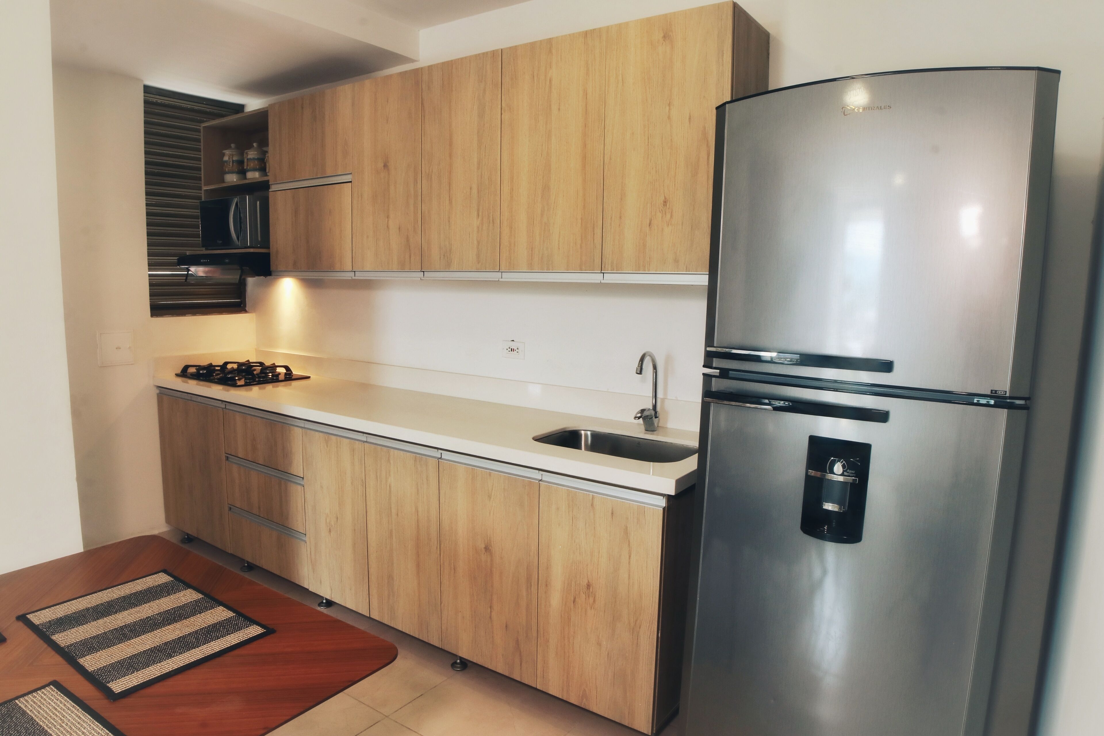 Eine moderne Küche mit Holzausstattung, einem Edelstahl-Kühlschrank, einer Mikrowelle und einem Gasherd.