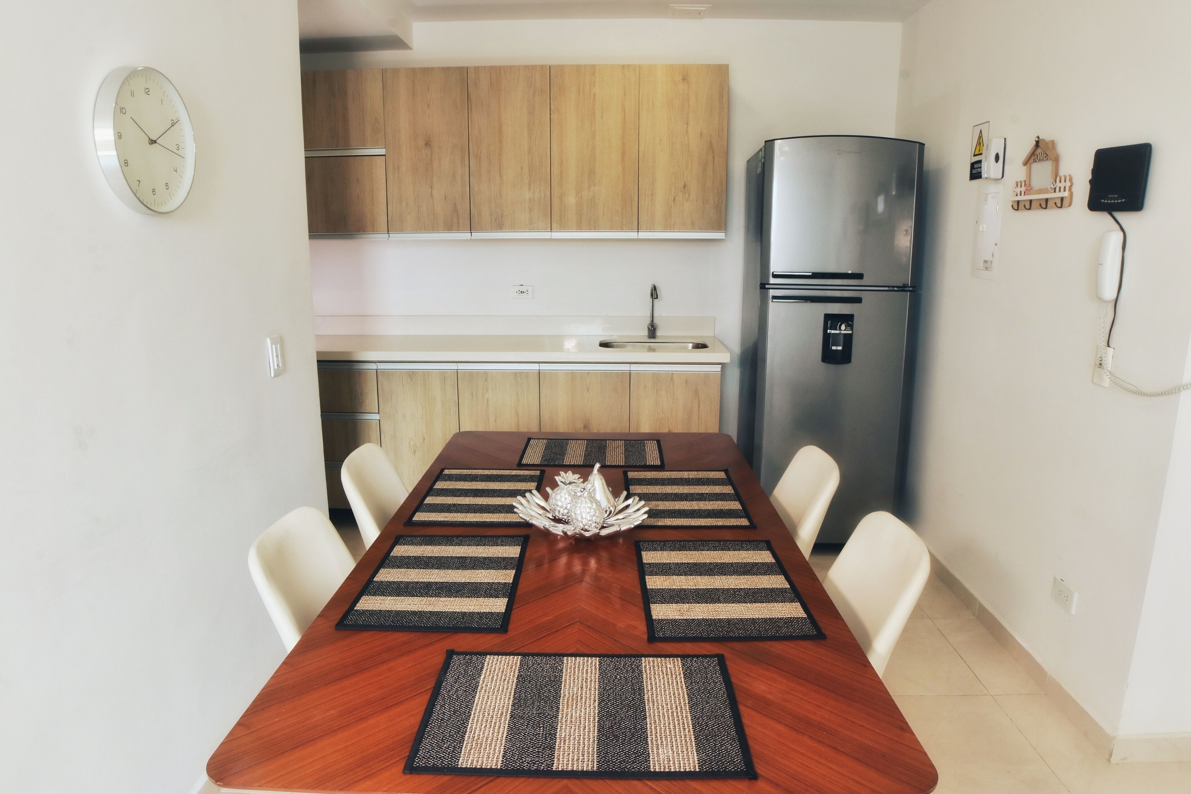 Eine moderne Küche mit Holdekor-Schränken, einem Edelstahl-Kühlschrank und einem Essbereich mit Holztisch und weißen Stühlen.
