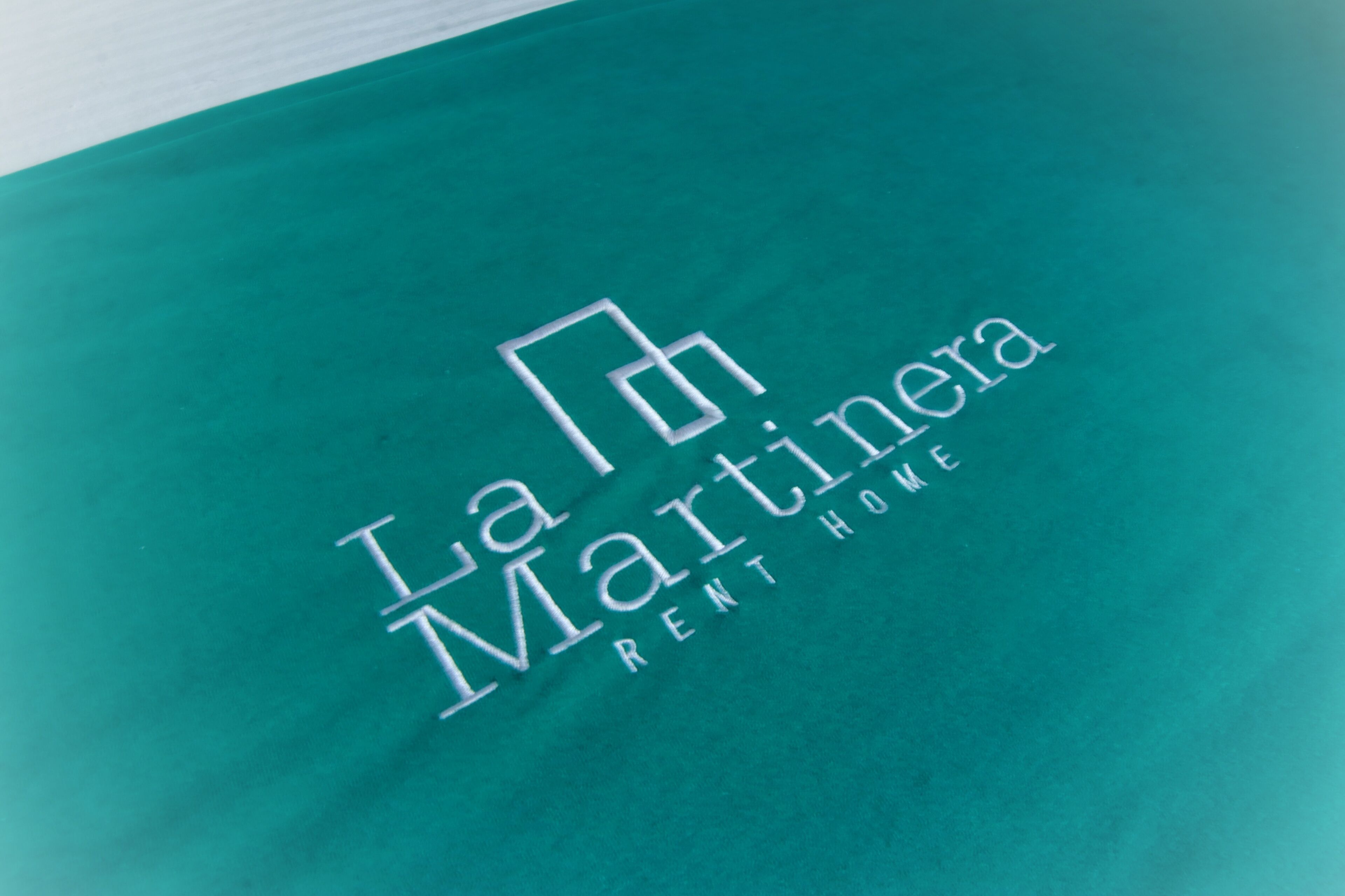A teal-colored fabric with the text "La Martinera RENT HOME" embossed on it.