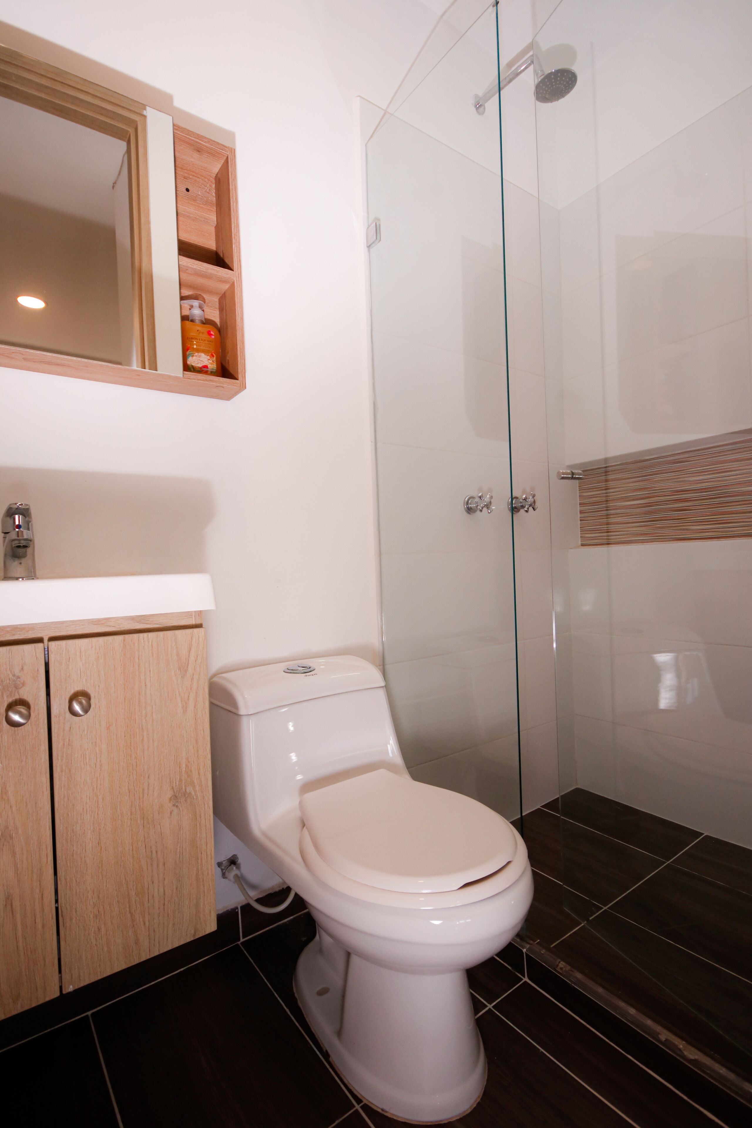 A modern bathroom with a toilet, a glass-enclosed shower, and a wooden cabinet with a mirror above the sink.