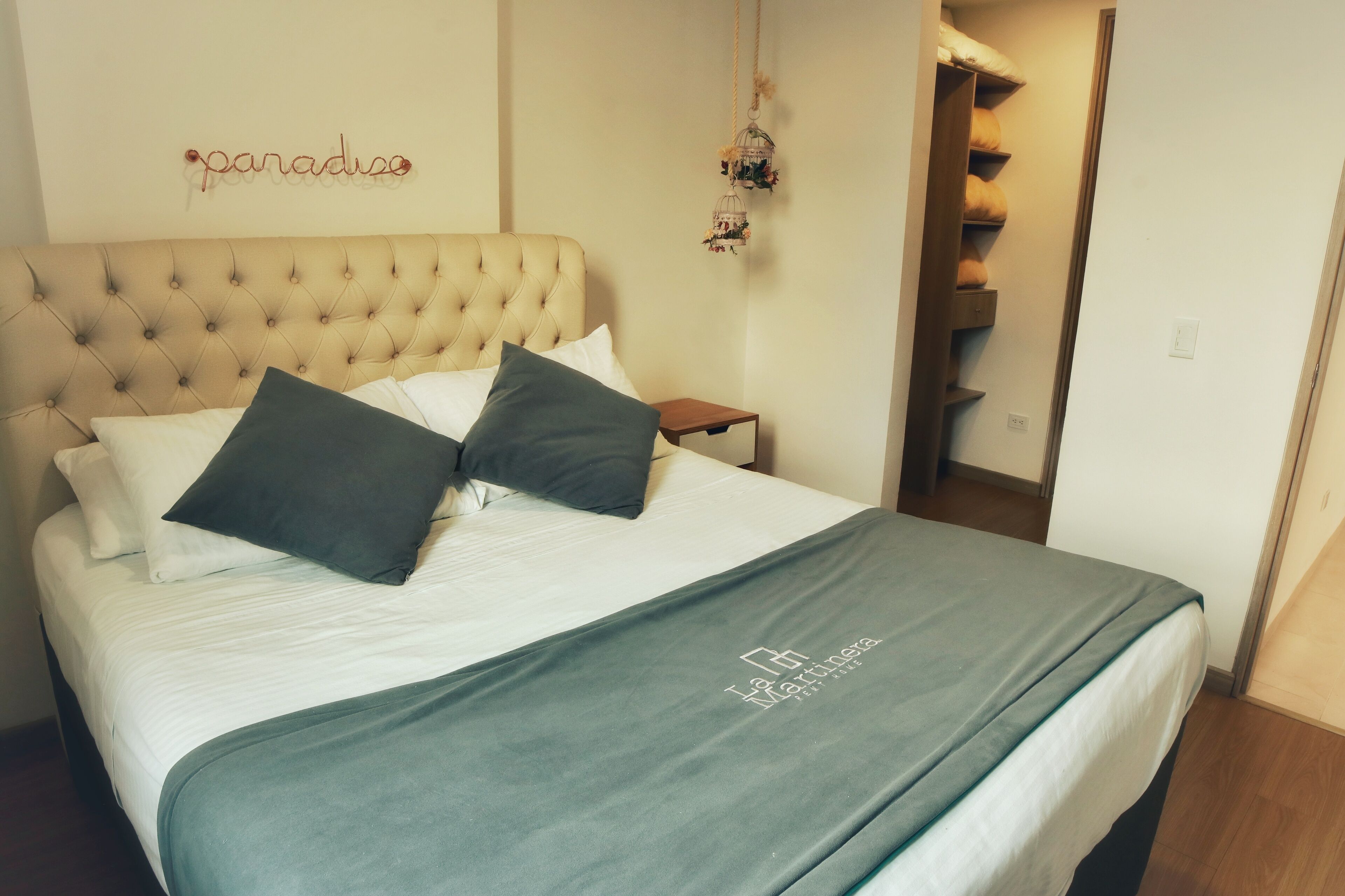 A neatly made bed with a tufted headboard, a green throw blanket, and two pillows. A small wooden nightstand is beside the bed.