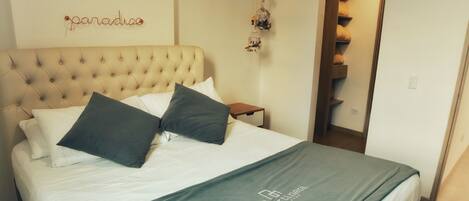 A neatly made bed with a tufted headboard, a green throw blanket, and two pillows. A small wooden nightstand is beside the bed.