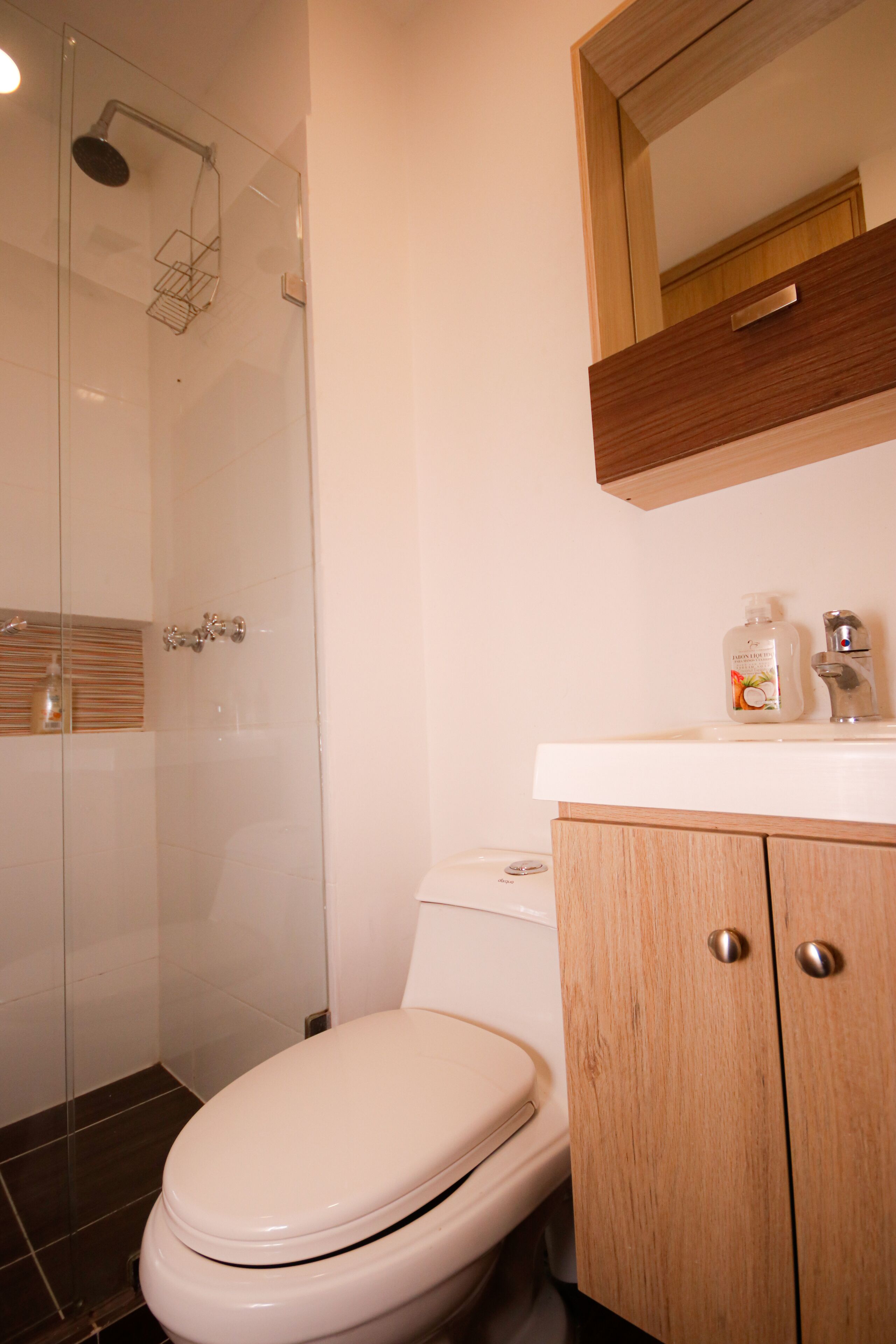 A bathroom with a glass shower enclosure, a white toilet, and wooden cabinets.