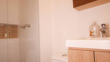 A bathroom with a glass shower enclosure, a white toilet, and wooden cabinets.