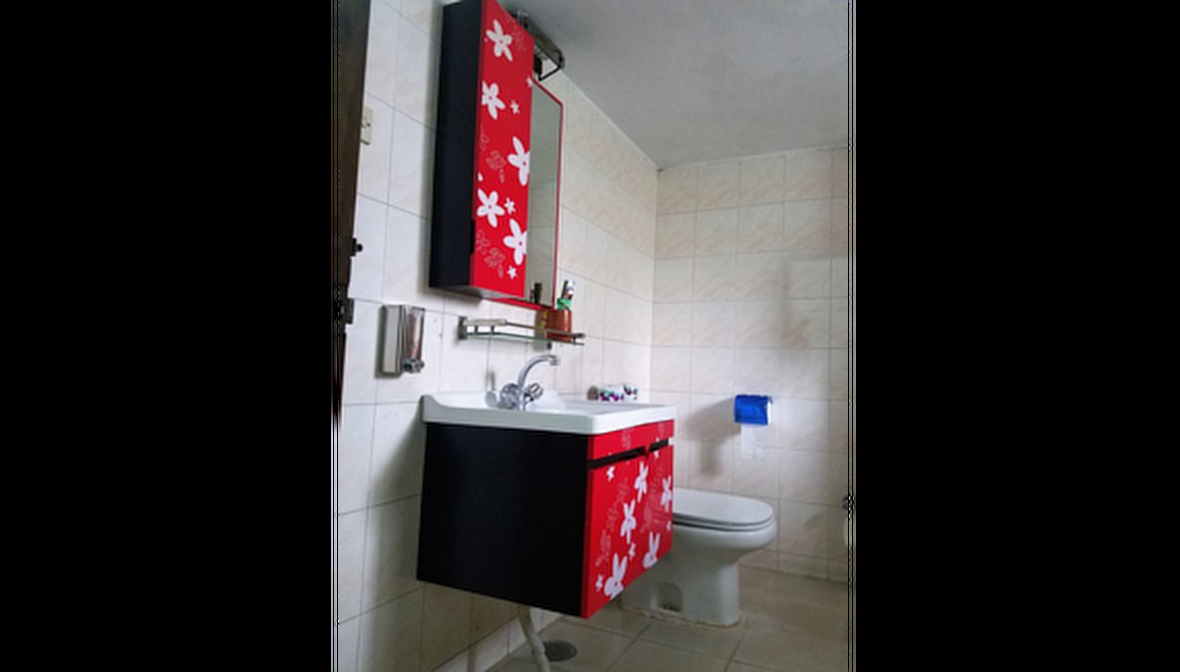 A bathroom with a white sink, a red and black cabinet, a mirror, and a toilet.