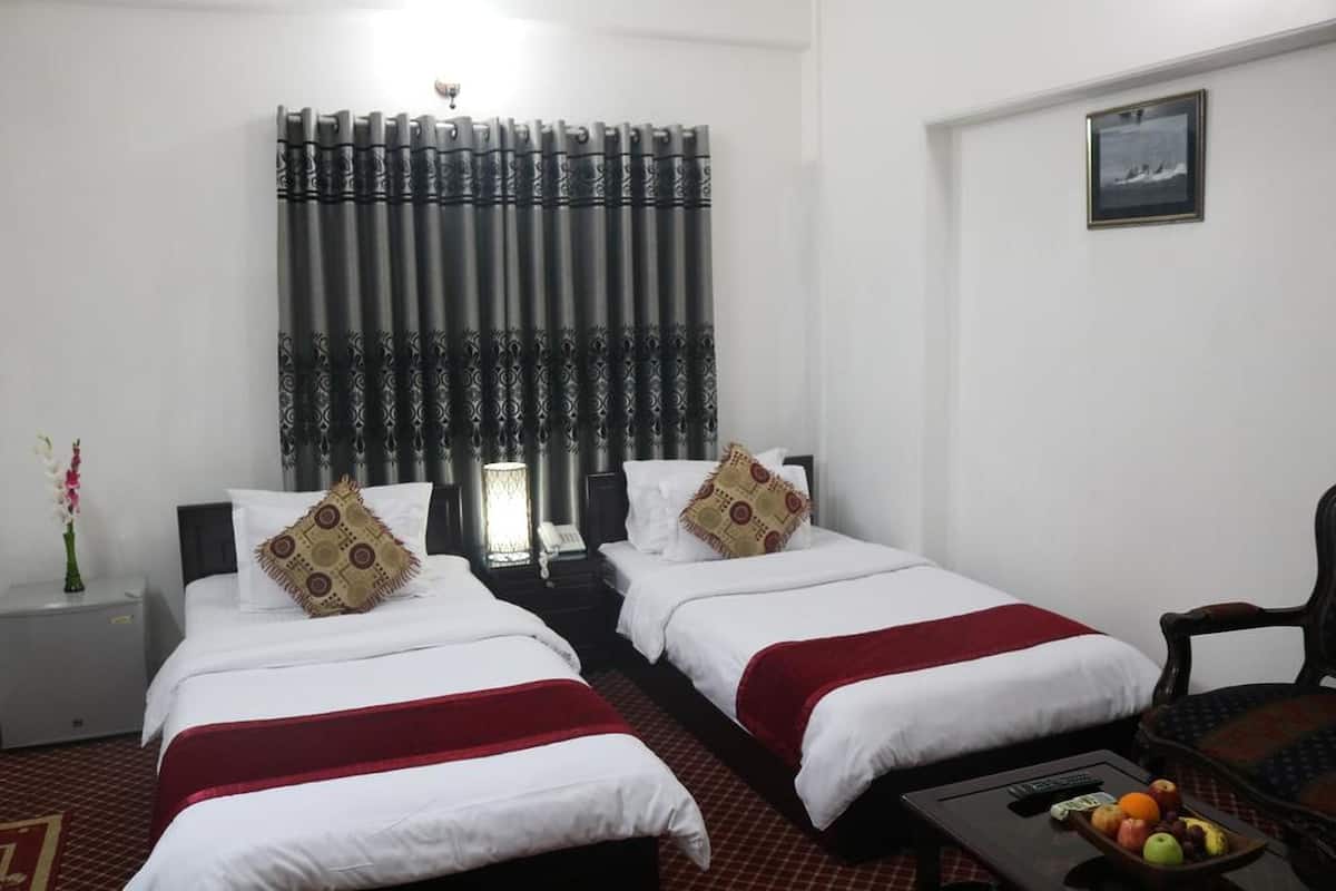 A hotel room with two beds, a nightstand, a lamp, a chair, and a table with fruits.