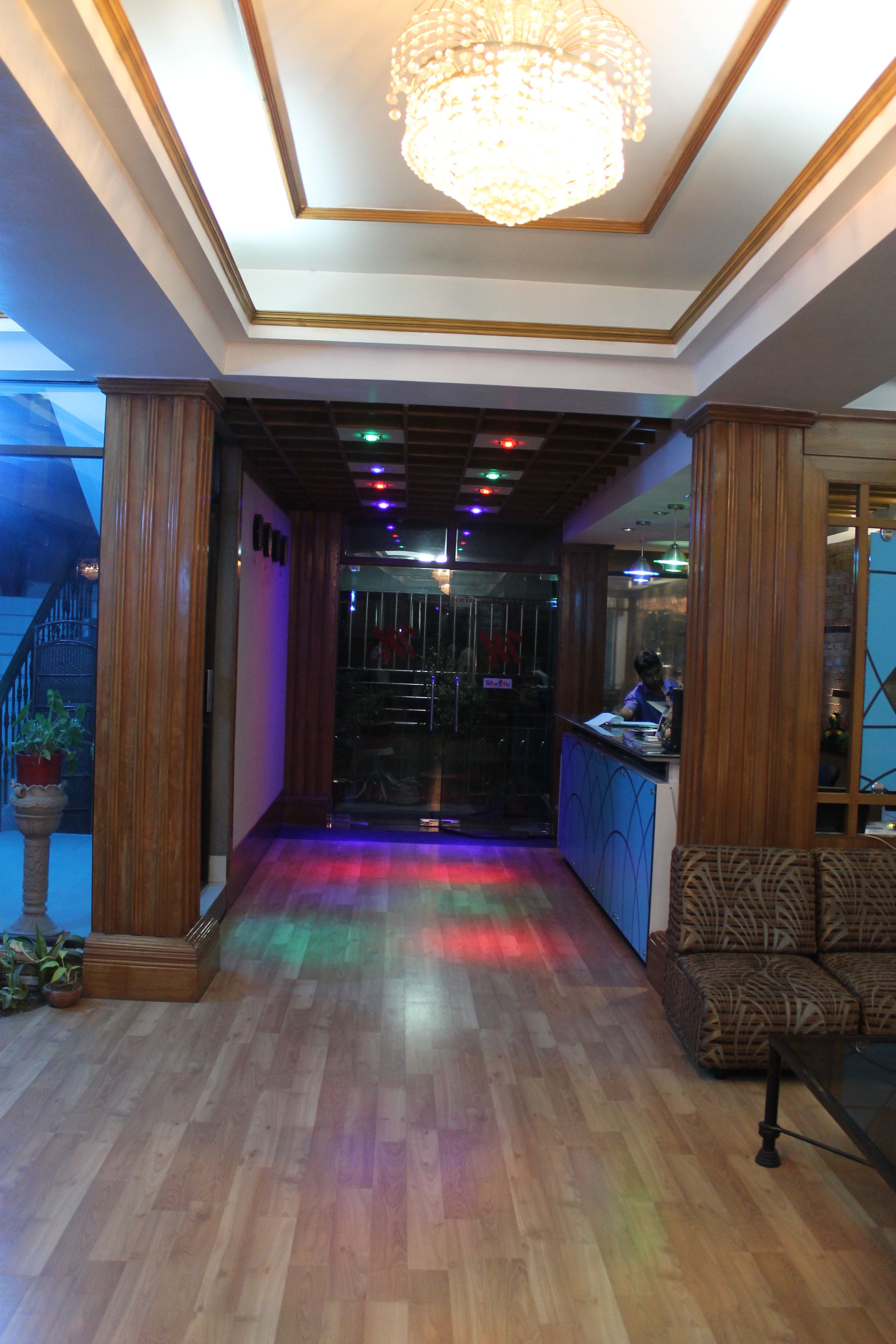 A hotel lobby with a wooden floor, a chandelier, a reception desk, and a patterned sofa.