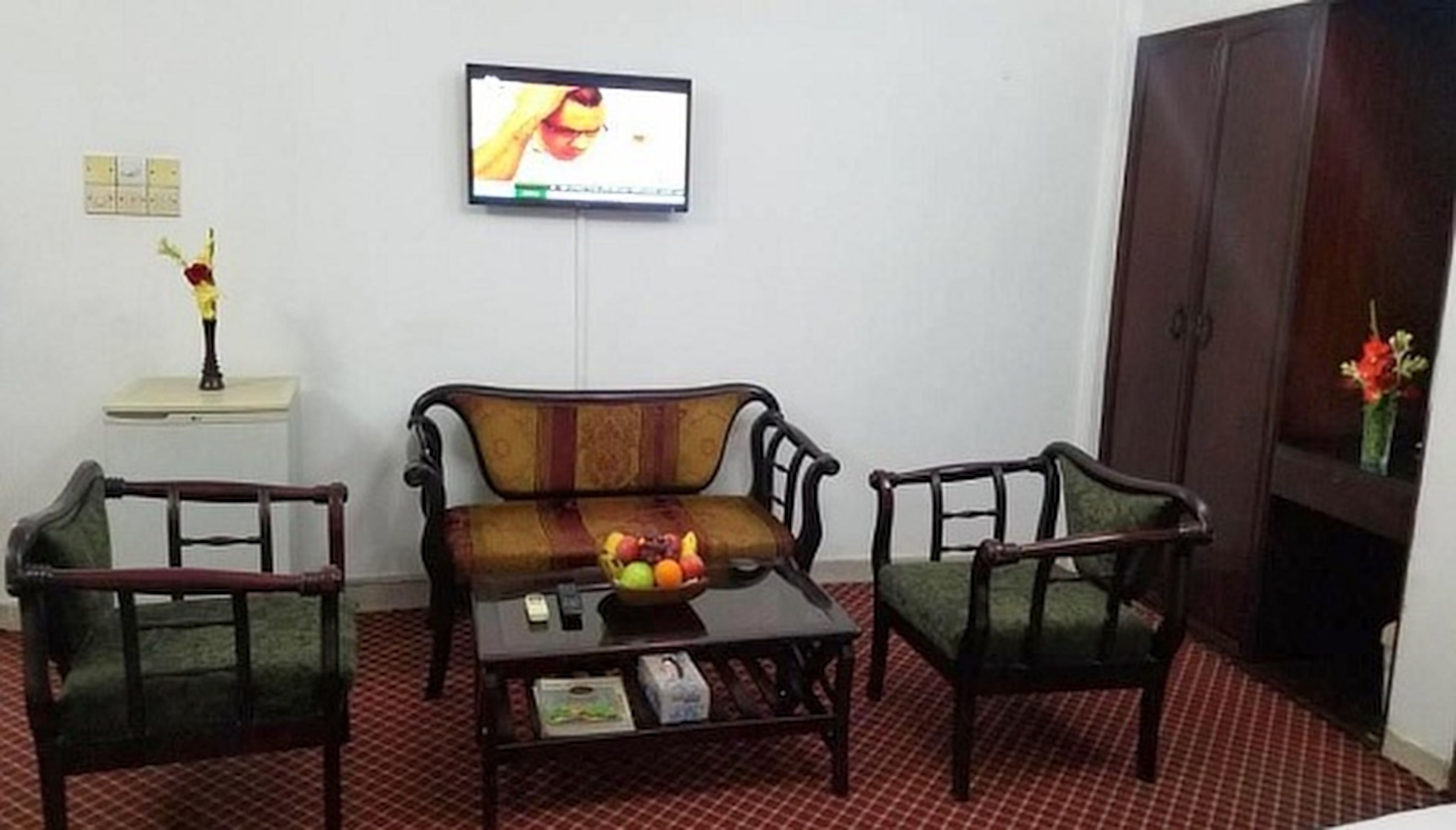 A room with a sofa, two armchairs, a coffee table with fruit, a television, and a cabinet.