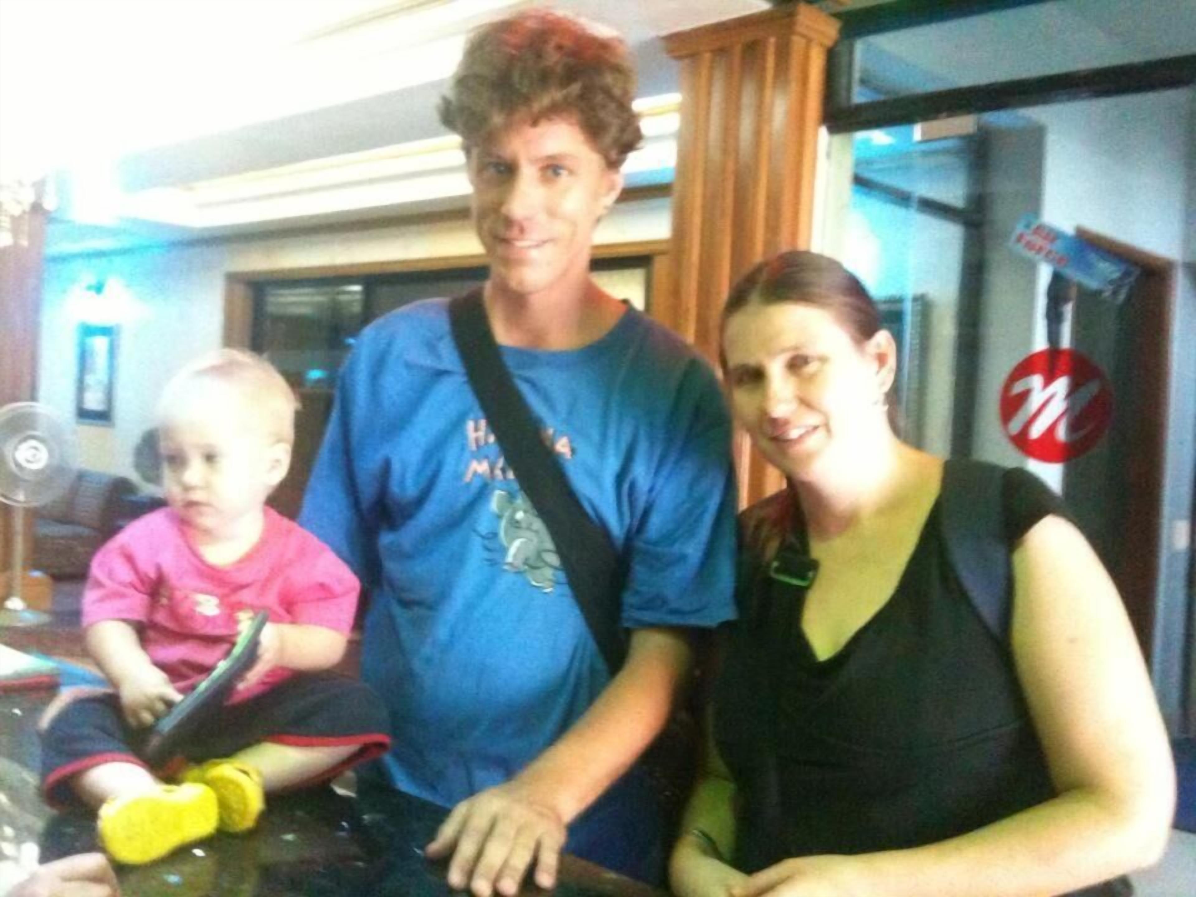 A hotel room with a glass table, a child in a pink shirt, an adult in a blue shirt, and a woman in a black dress.