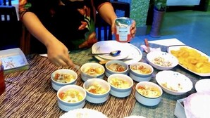 A woman seated at a table with multiple bowls of food, a plate with a drink, and a potted plant in the background. - Hotel De Meridian (Dhaka)