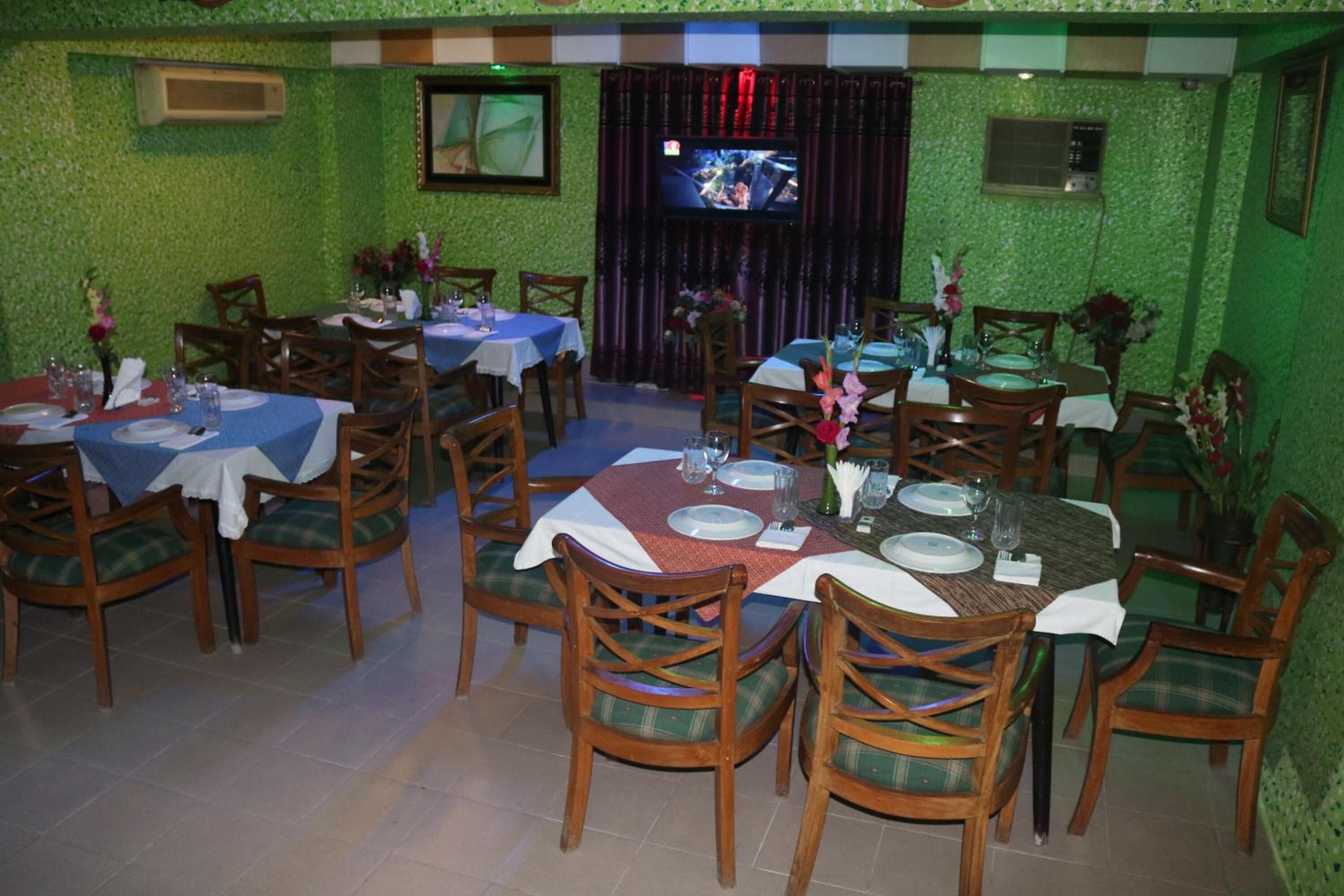 Un restaurante con varias mesas y sillas, paredes verdes y una pantalla de televisión.